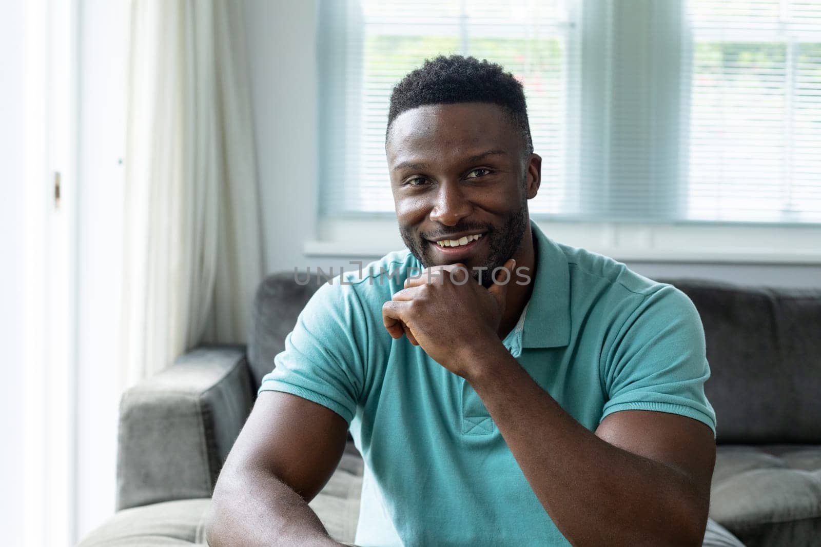 Portrait of smiling afrcian american young man with hand on chin at home by Wavebreakmedia