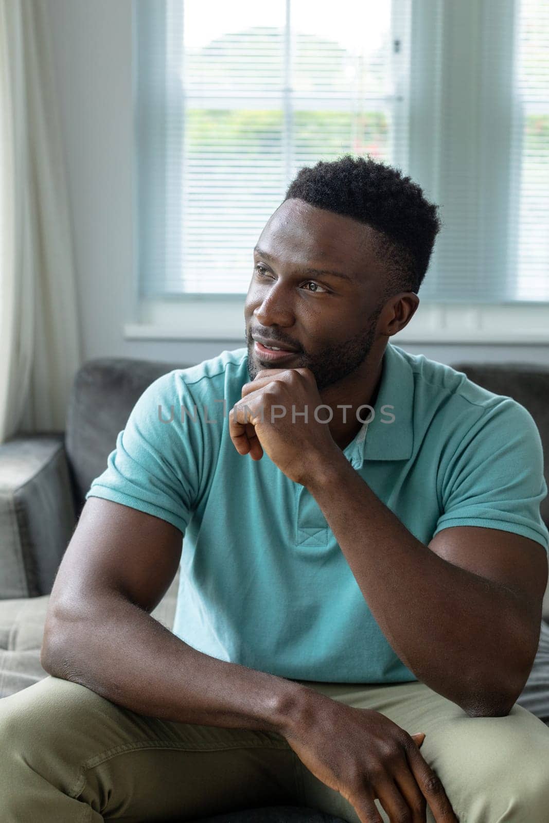 Thoughtful afrcian american young man with hand on chin at home by Wavebreakmedia