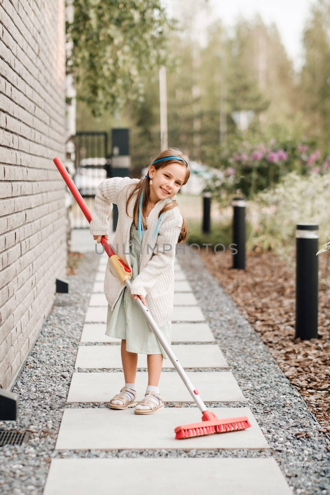 A little girl with a brush cleans a path on the street in the courtyard by Lobachad