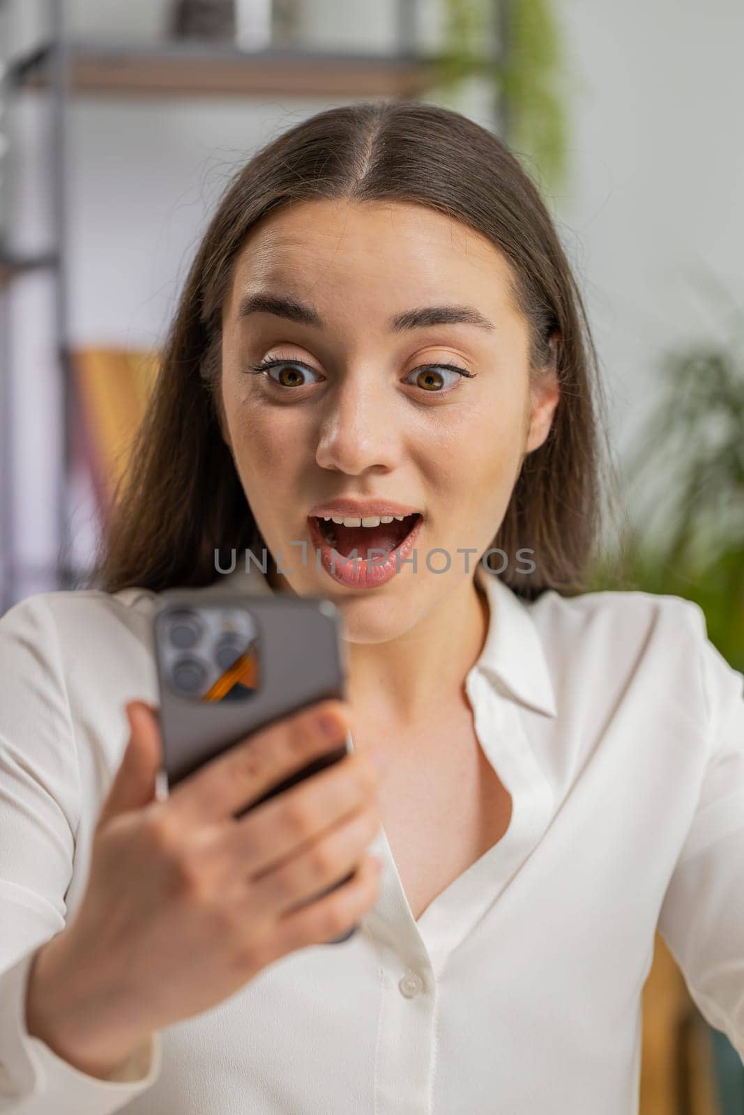 Oh my God, Wow. Happy amazed young business woman working on smartphone shocked by sudden victory, game winning, lottery goal achievemen good news. Pretty manager girl freelancer at office. Vertical