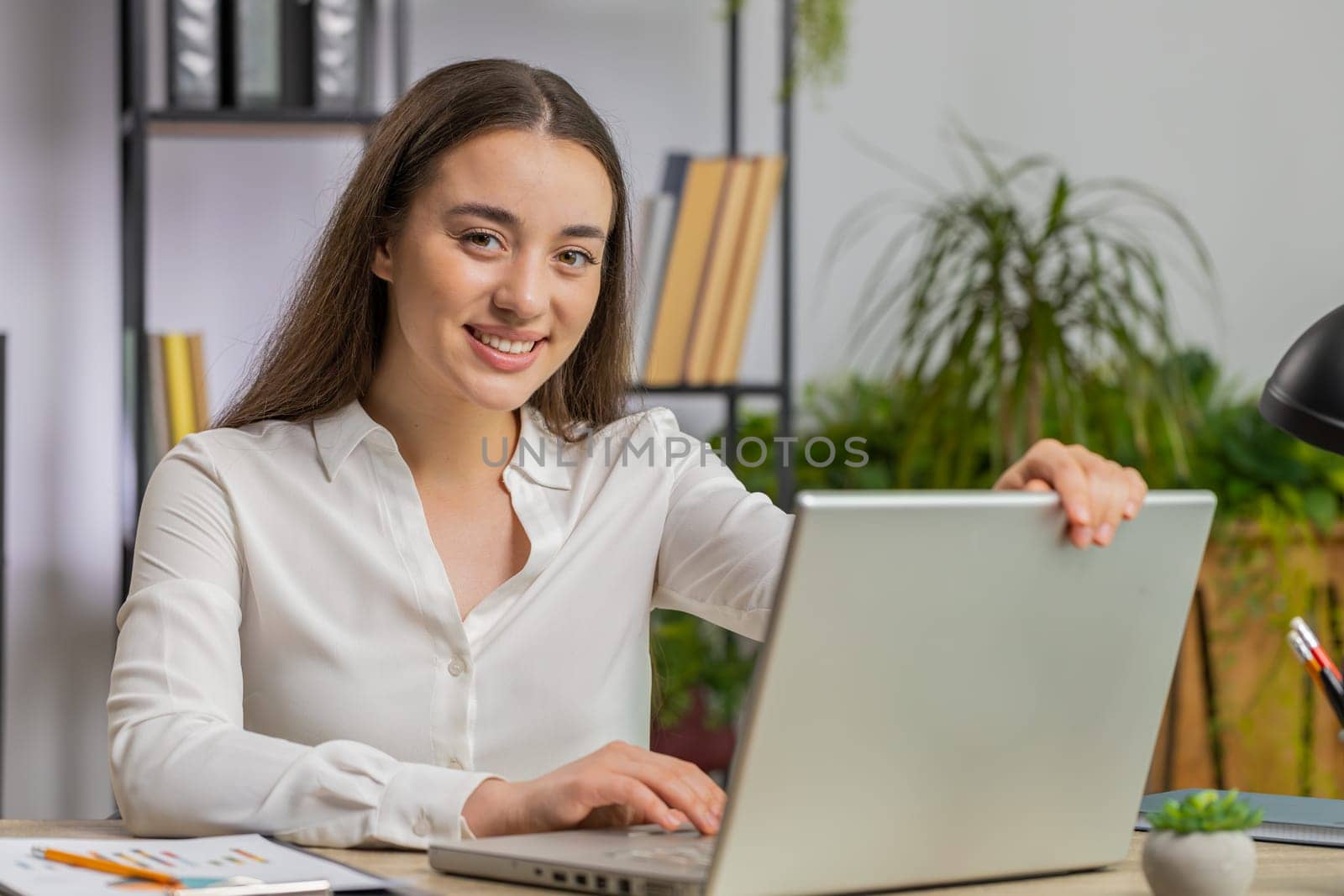 Caucasian young business woman freelancer at office workplace start working on laptop computer. Professional broker freelancer girl opens notebook sends messages makes online purchases watching movies