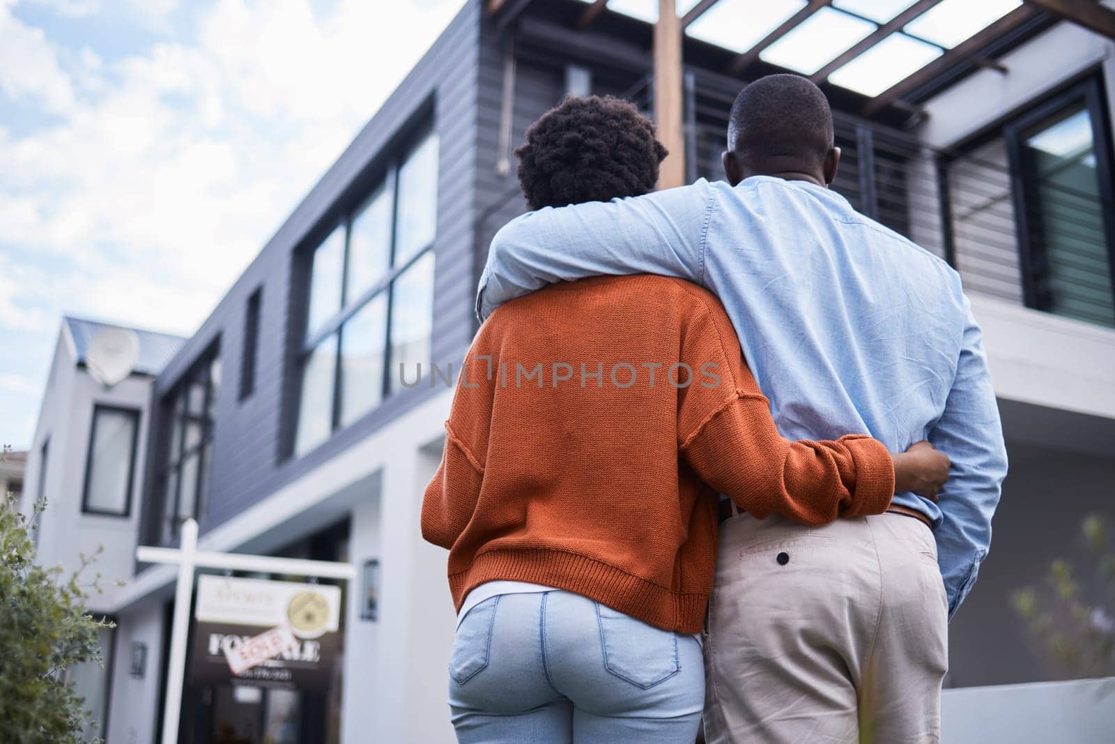 Love, hugging and back of couple by their new home, property or real estate standing together. Relocation, romance and behind of an African man and woman homeowners embracing by their modern house