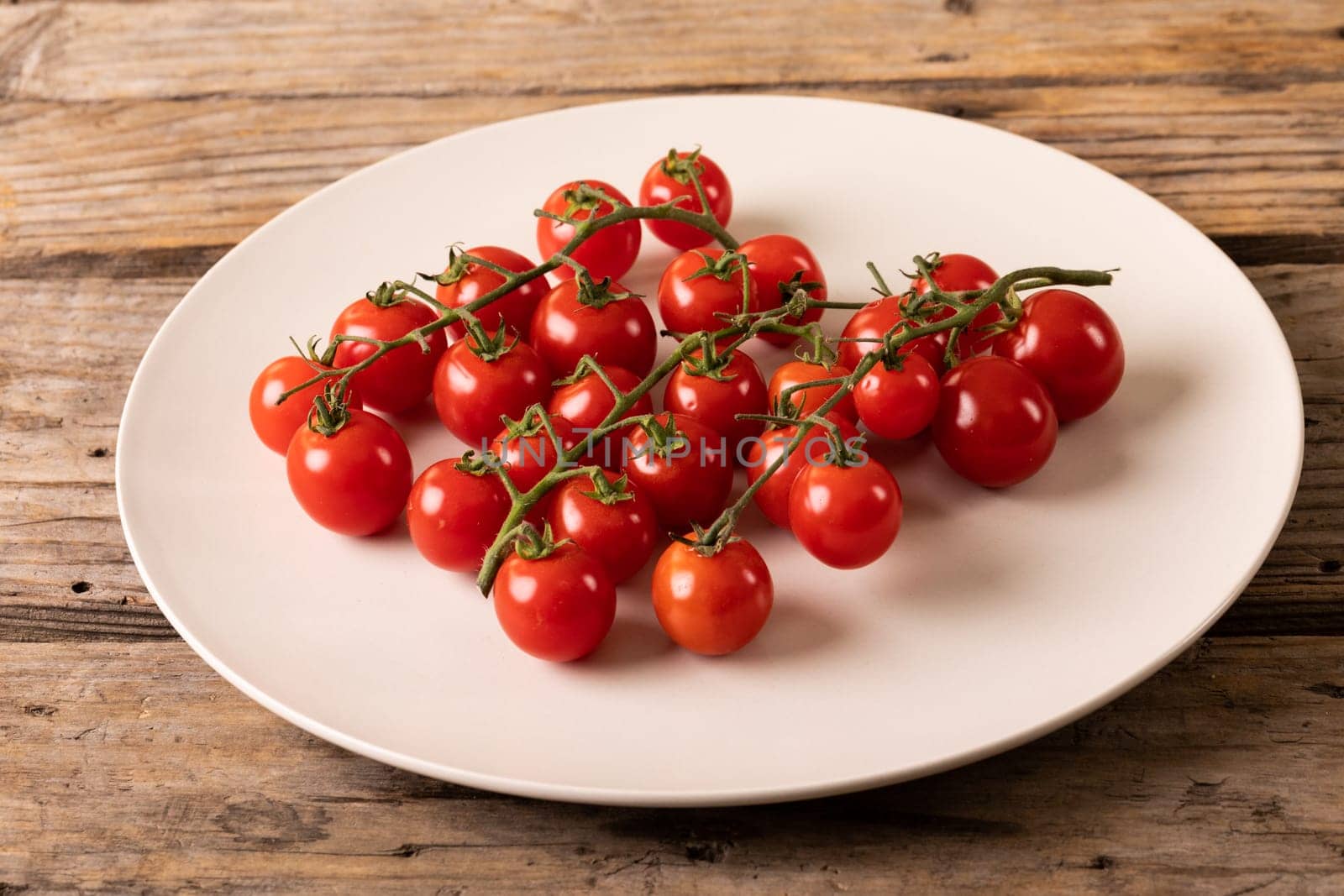 High angle view of fresh red cherry tomatoes in white plate on wooden table. unaltered, organic food and healthy eating concept.