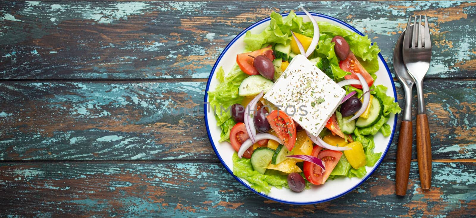 Traditional Greek Salad with Feta Cheese, Tomatoes, Bell Pepper, Cucumbers, Olives, Herbs in white ceramic bowl on blue rustic wooden table background from above, Cuisine of Greece. Copy Space by its_al_dente