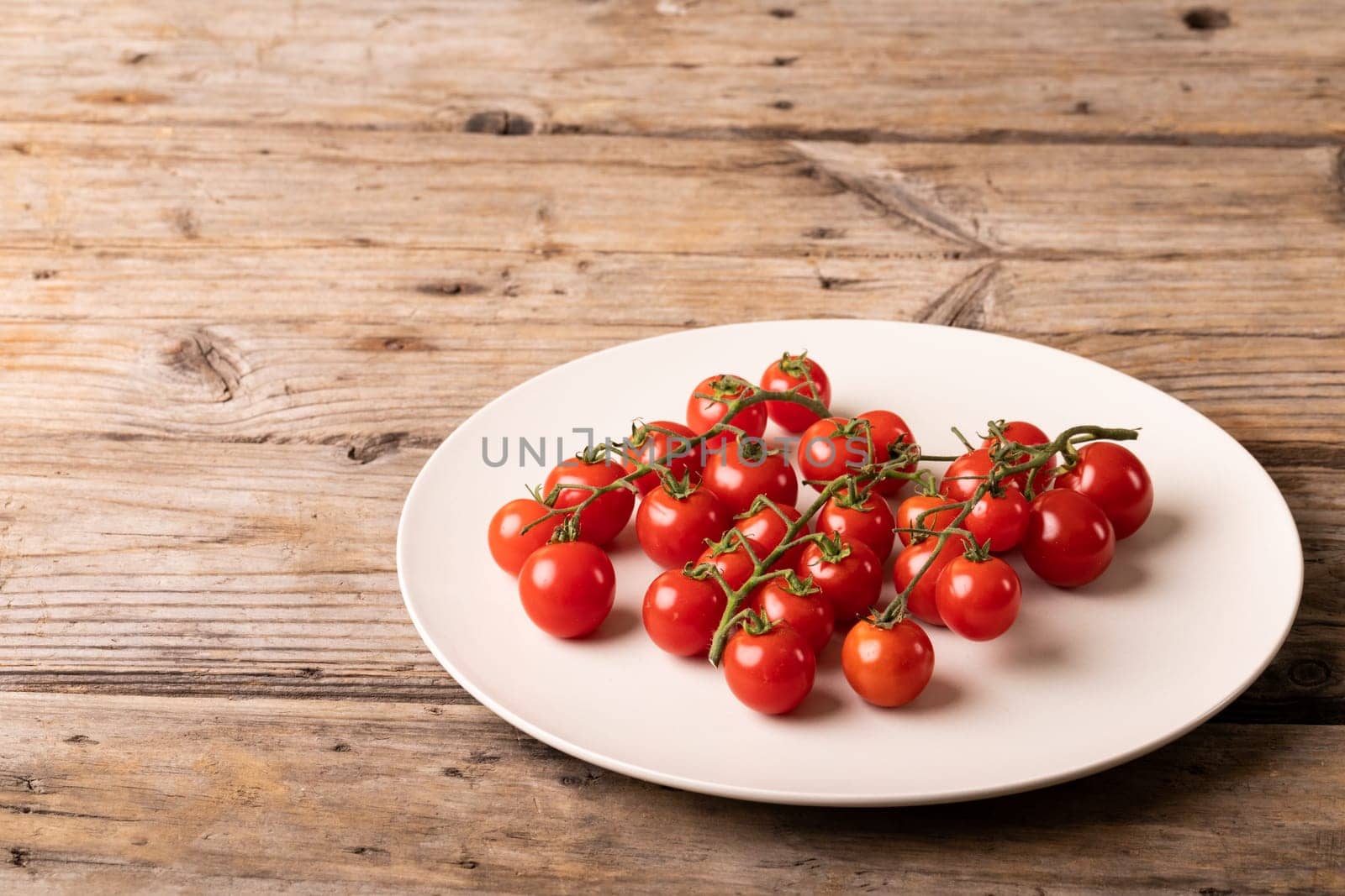 High angle view of fresh red cherry tomatoes in plate on brown wooden table. unaltered, organic food and healthy eating concept.