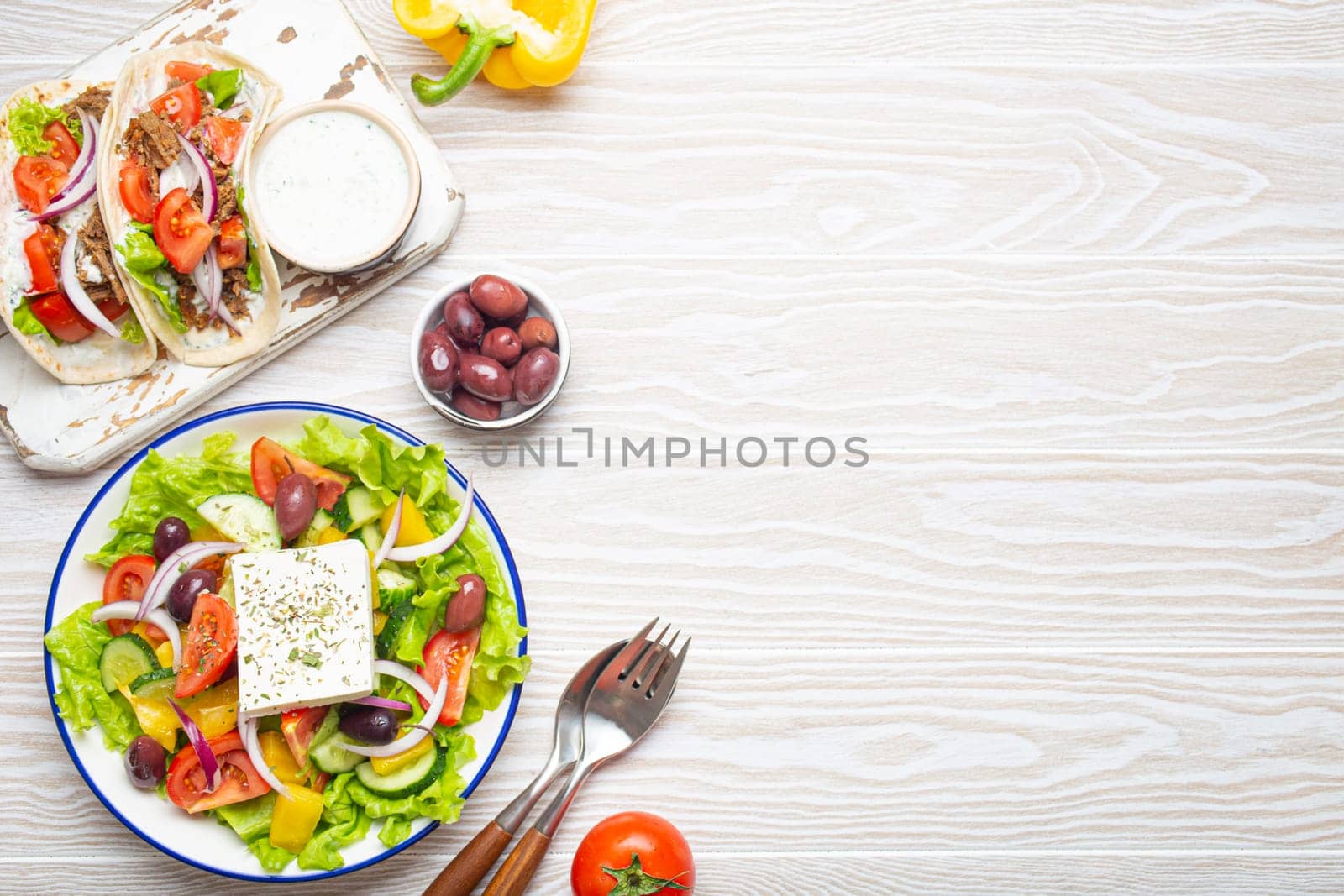 Traditional Greek Food: Greek Salad, Gyros with meat and vegetables, Tzatziki sauce, Olives on White rustic wooden table background from above. Cuisine of Greece. Copy space