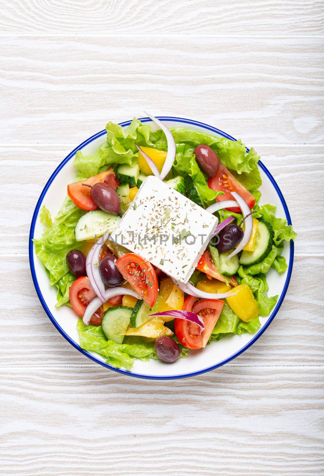 Traditional Greek Salad with Feta Cheese, Tomatoes, Bell Pepper, Cucumbers, Olives, Herbs in white ceramic bowl on White rustic wooden table background top view, Cuisine of Greece by its_al_dente