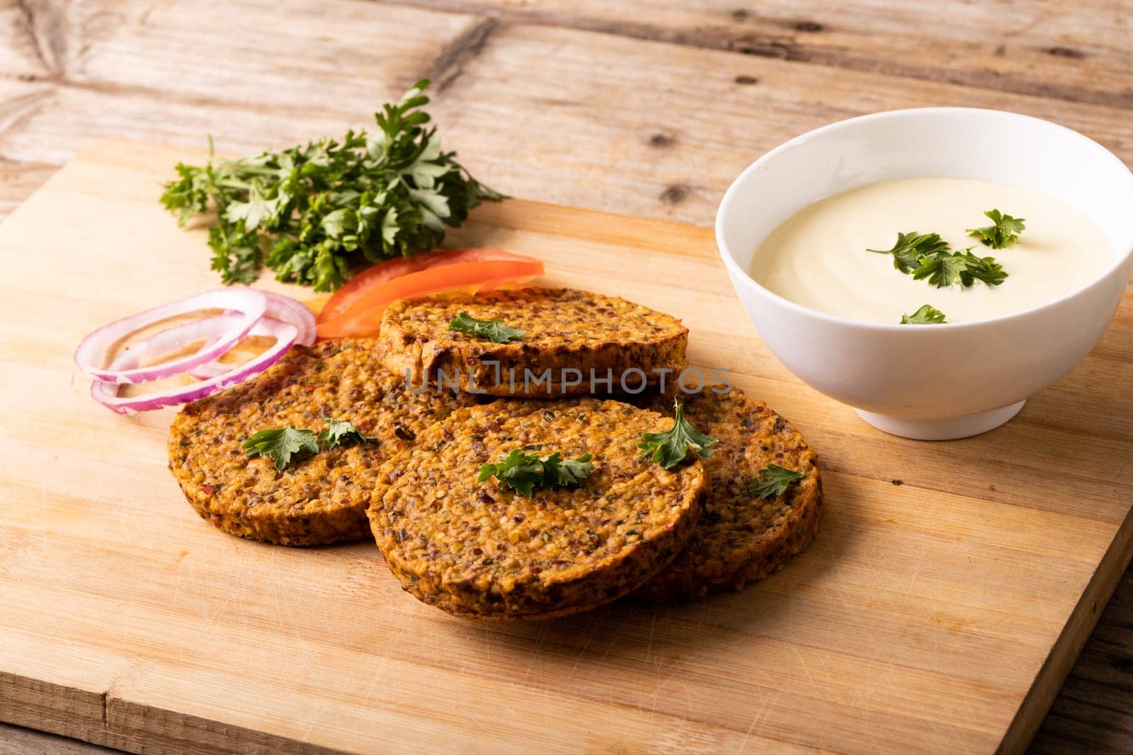 High angle view of fresh patties with dip bowl served on wooden serving board by Wavebreakmedia