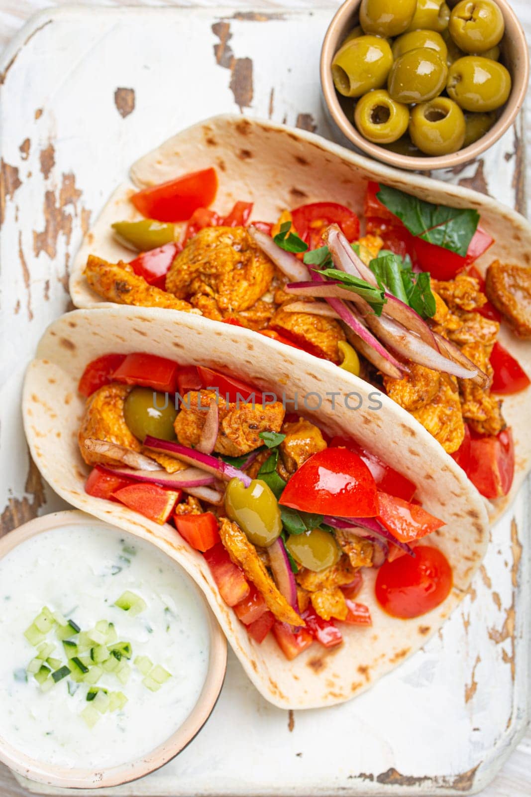 Traditional Greek Dish Gyros: Pita bread Wraps with vegetables, meat, herbs, olives on rustic wooden cutting board with Tzatziki sauce, olive oil top view on white wooden background, closeup. by its_al_dente