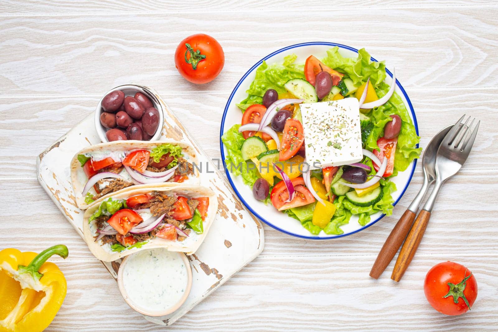 Traditional Greek Food: Greek Salad, Gyros with meat and vegetables, Tzatziki sauce, Olives on White rustic wooden table background top view. Cuisine of Greece