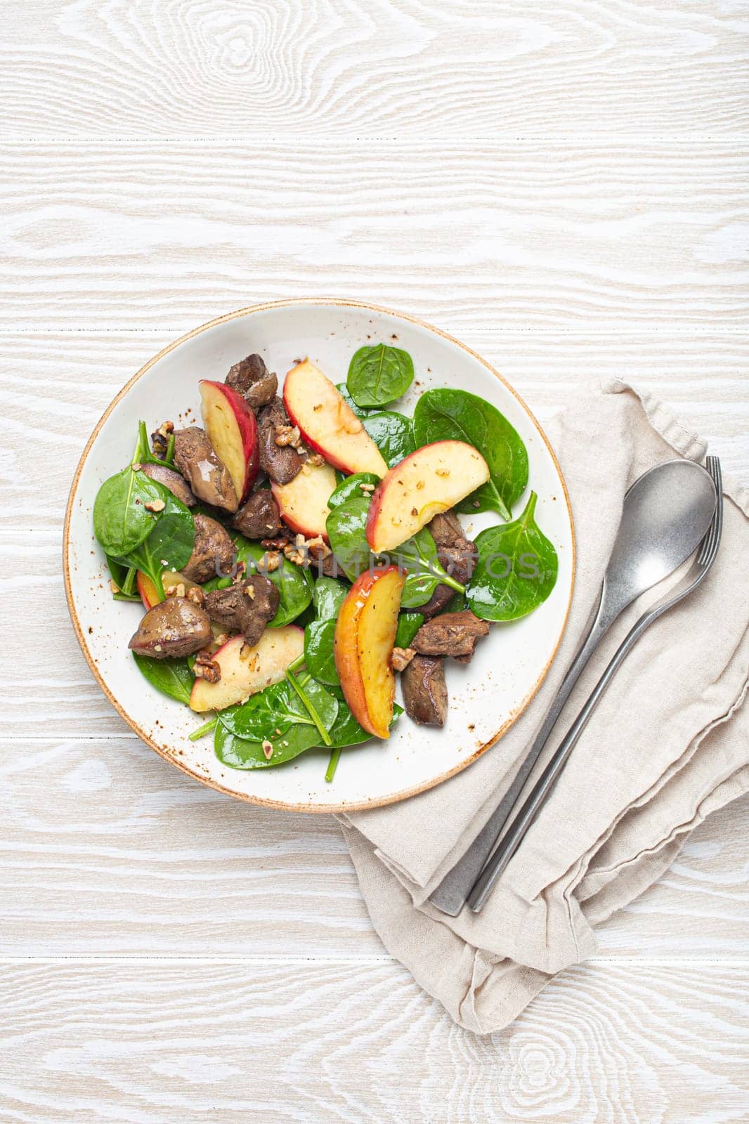 Healthy Salad with Iron Rich Ingredients Chicken Liver, Apples, Fresh Spinach and Walnuts on White Ceramic Plate, White Wooden Background From Above.