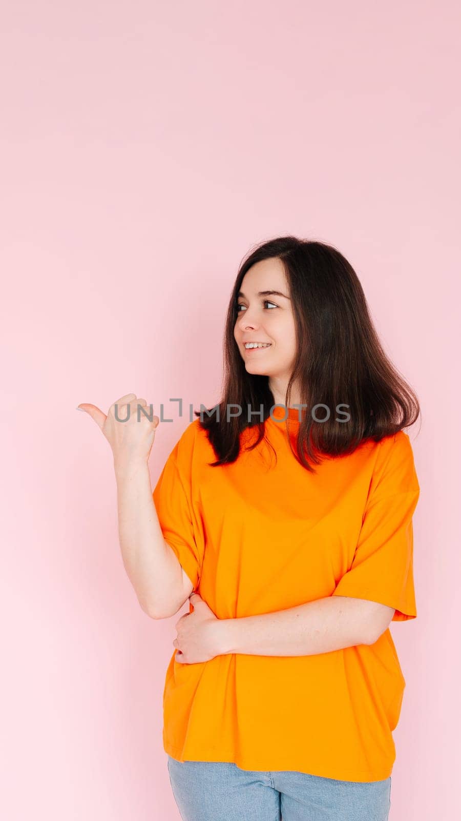 Alluring Advertising Space: Charming Lady Pointing Thumbs at Empty Area - Attention-Grabbing Concept for Promotional Opportunities on Pink Background