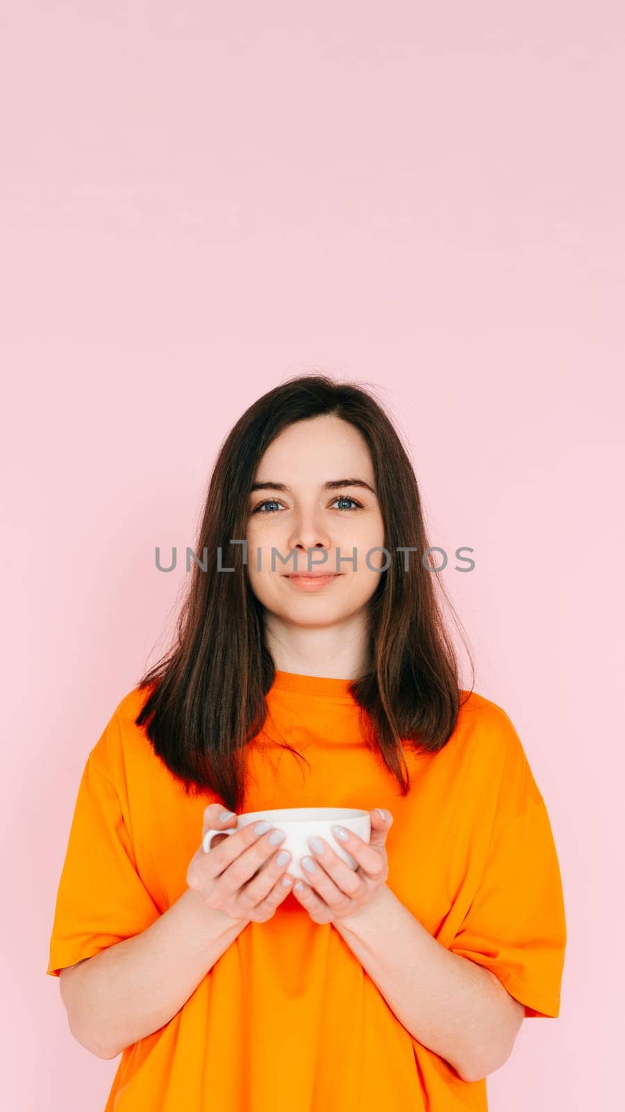 Serene Leisure: Charming Woman in Orange Attire, Savoring a Delightful Drink in a Mug - Relishing Free Time After Work, Tranquility and Bliss Isolated on Pink Background.
