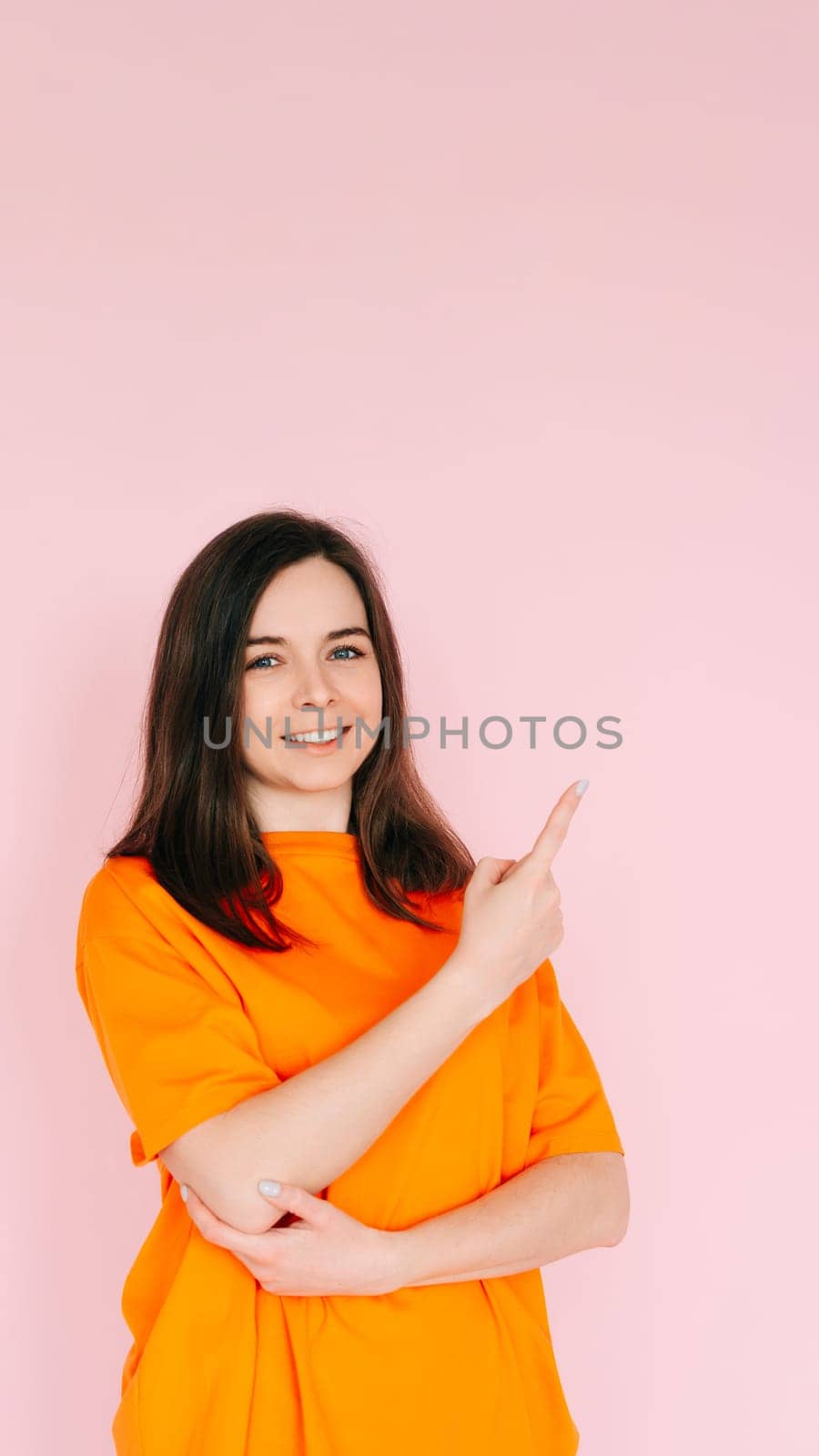 Playful Gestures: Charming Woman Pointing Finger at Empty Space - Humor and Interaction Concept, Isolated on Pink Background