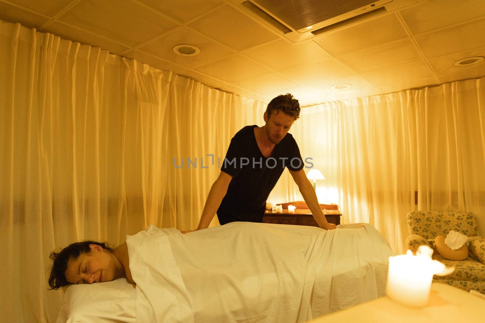 Massage session - master relaxes the body of the female client through a white cloth. Mid shot