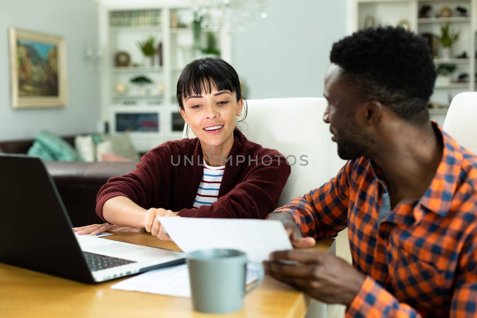 Multiracial young couple with laptop discussing household expense budget over bill at home. unaltered, lifestyle, togetherness, finance, planning, calculating, savings.