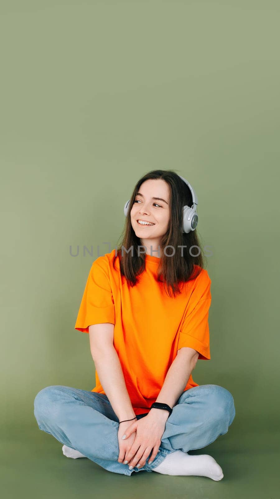 Portrait of a dreamy woman with headphones looking into the distance, isolated on a vibrant green background.