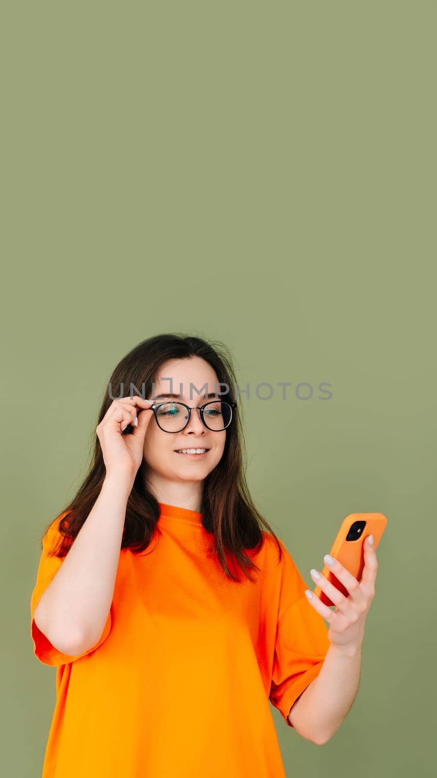 Picture of a cheerful young woman in an orange T-shirt using a modern smartphone in empty green space - technology and communication concept. isolated on green background with copy space for text.