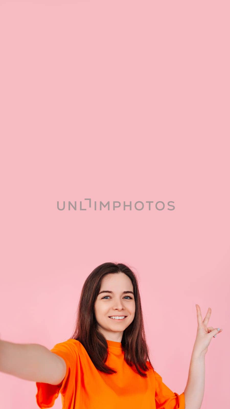 A vivaciously stunning girl with a radiant smile, confidently showing the V sign with her fingers. On a pink background. Blank space to add text or graphics for party, holiday and promotional design.