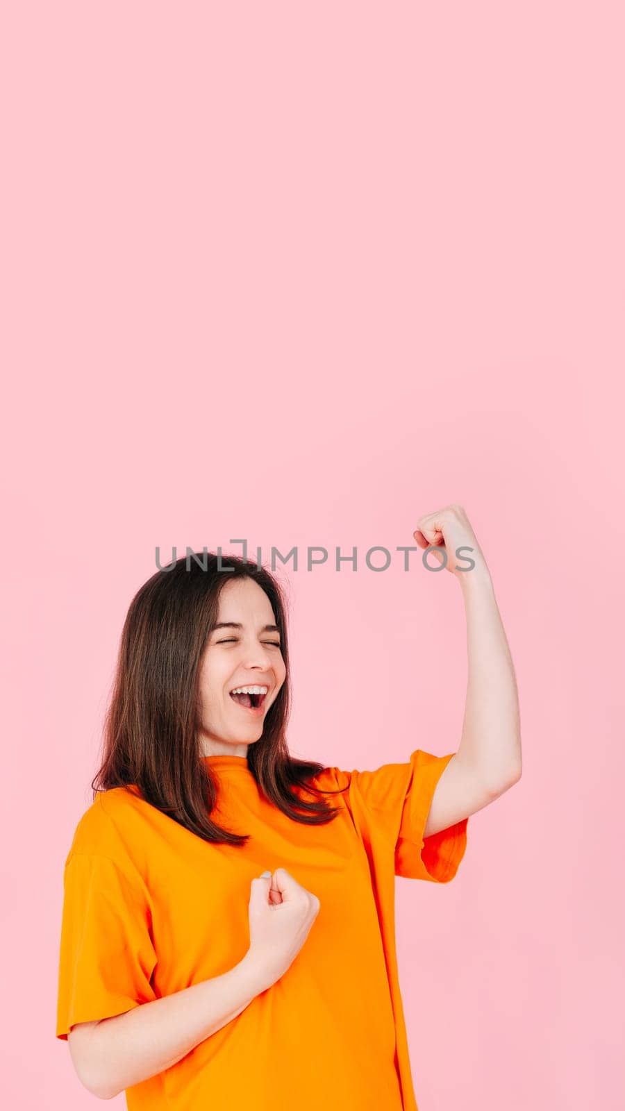 Triumphant Elation: Young Woman with Exuberant Expression, Raised Fists, Celebrating Success in Business. Vibrant Energy, Achievement, and Victory Concept. Isolated on Pink Background