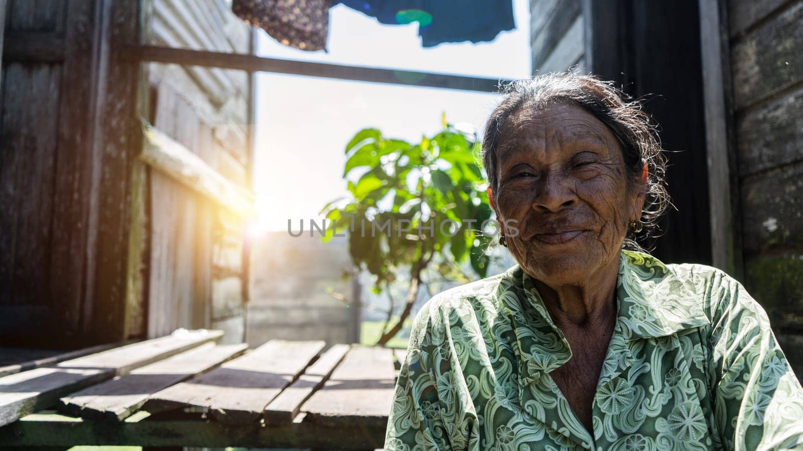 Close-up of an elderly indigenous woman in ordinary clothes sitting in her wooden hut at dawn