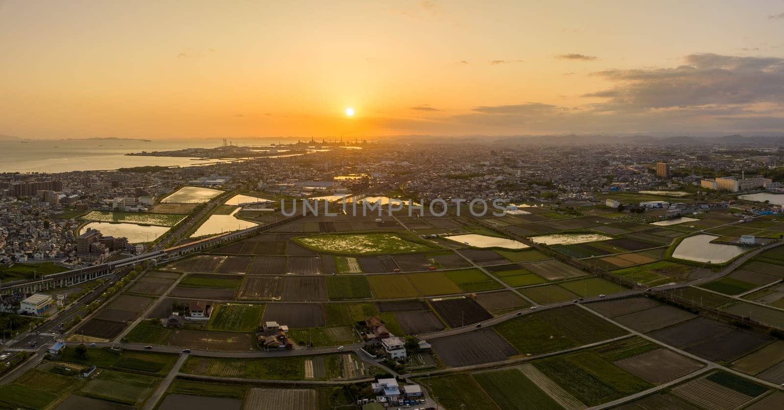 Aerial view of low sun in sky over fields at edge of small city on coast. High quality photo