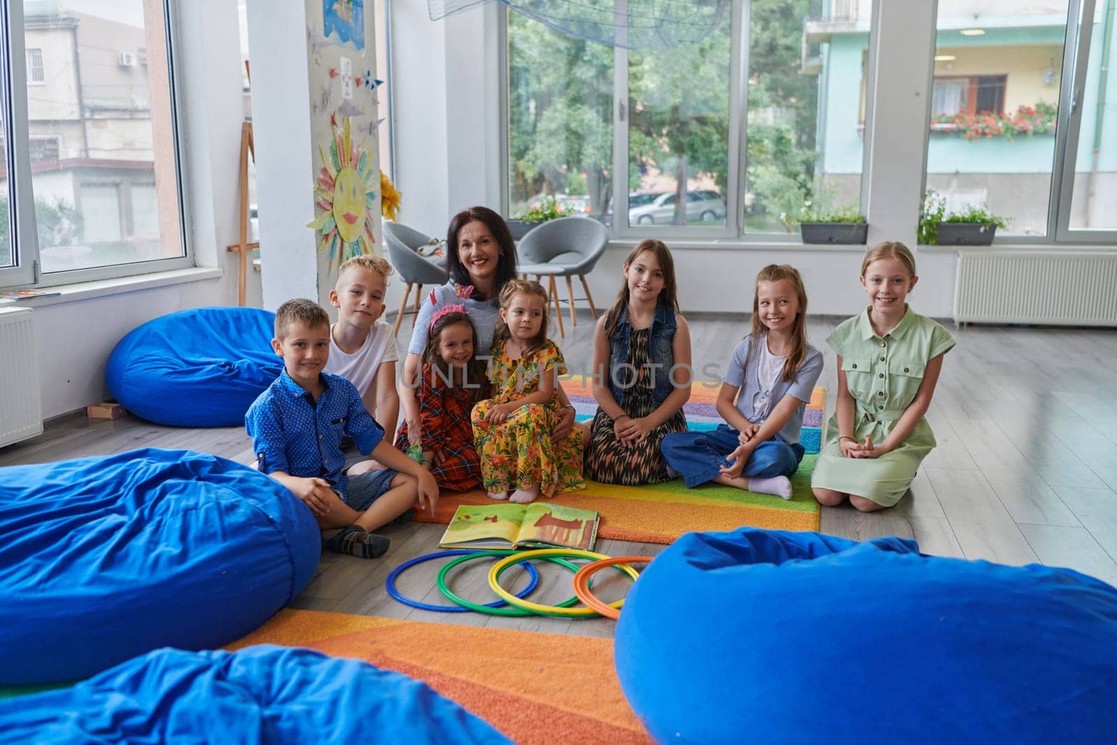 A happy female teacher sitting and playing hand games with a group of little schoolchildren.