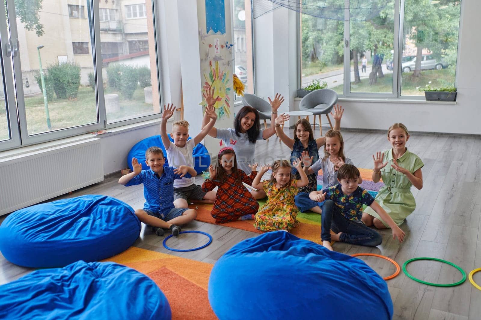 A happy female teacher sitting and playing hand games with a group of little schoolchildren.