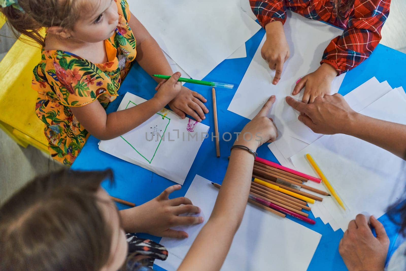 Creative kids during an art class in a daycare center or elementary school classroom drawing with female teacher