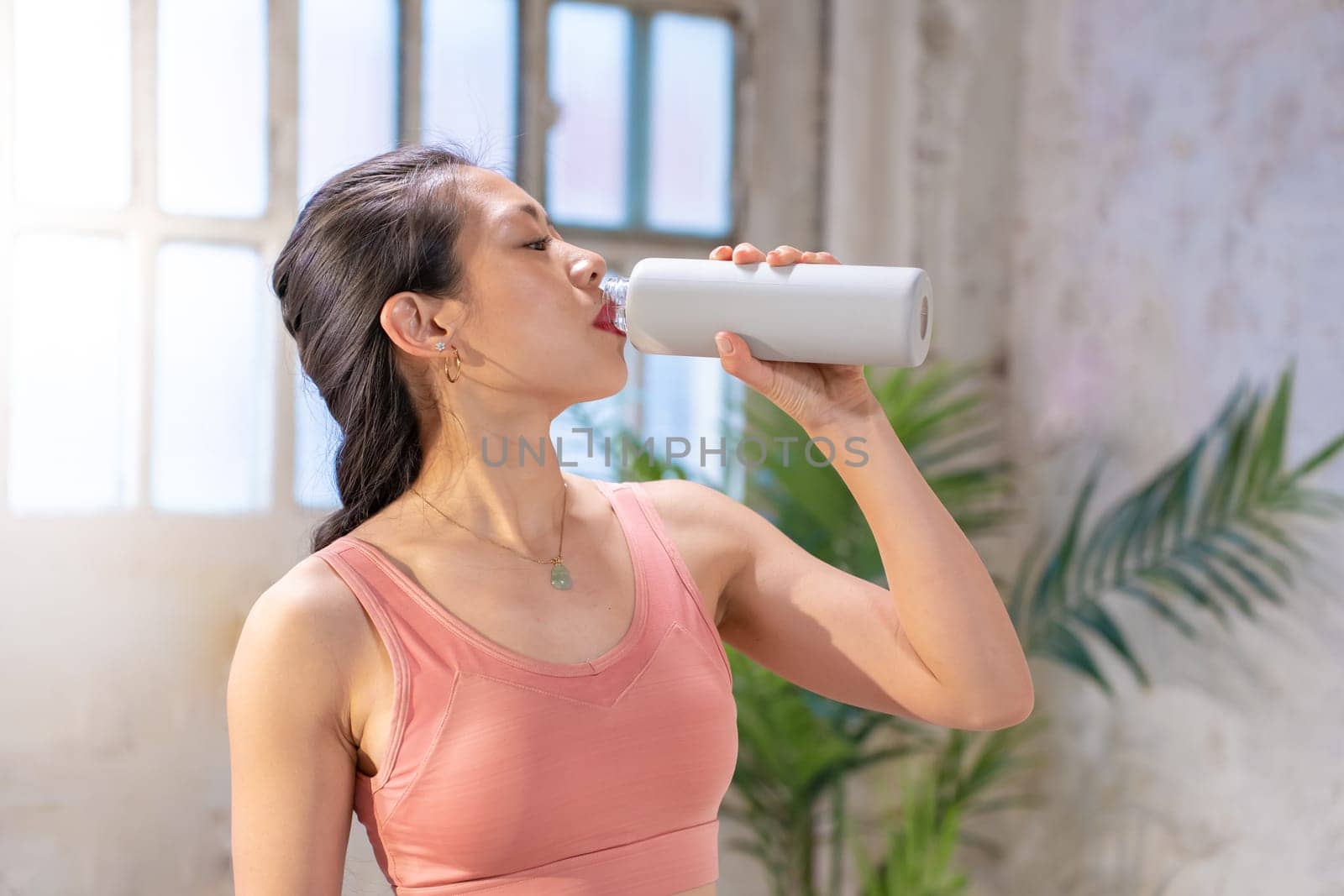 Beautiful sporty asian woman drinking water from a canteen. Healthy lifestyle concept. High quality photo