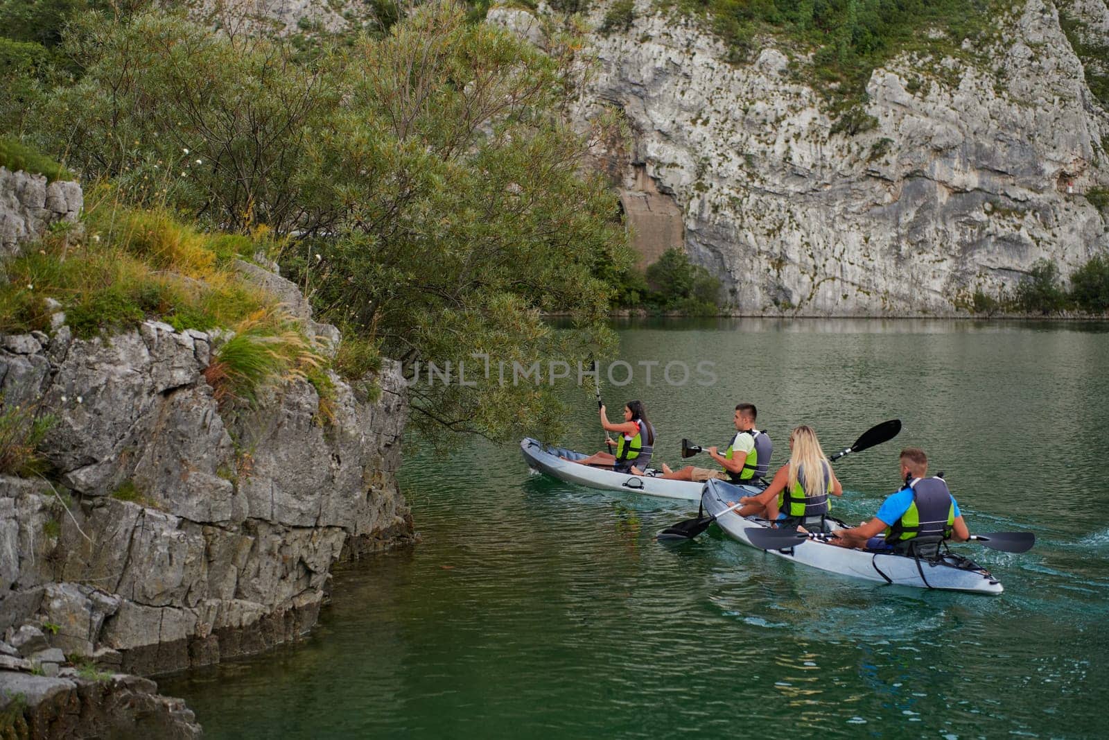 A group of friends enjoying having fun and kayaking while exploring the calm river, surrounding forest and large natural river canyons.