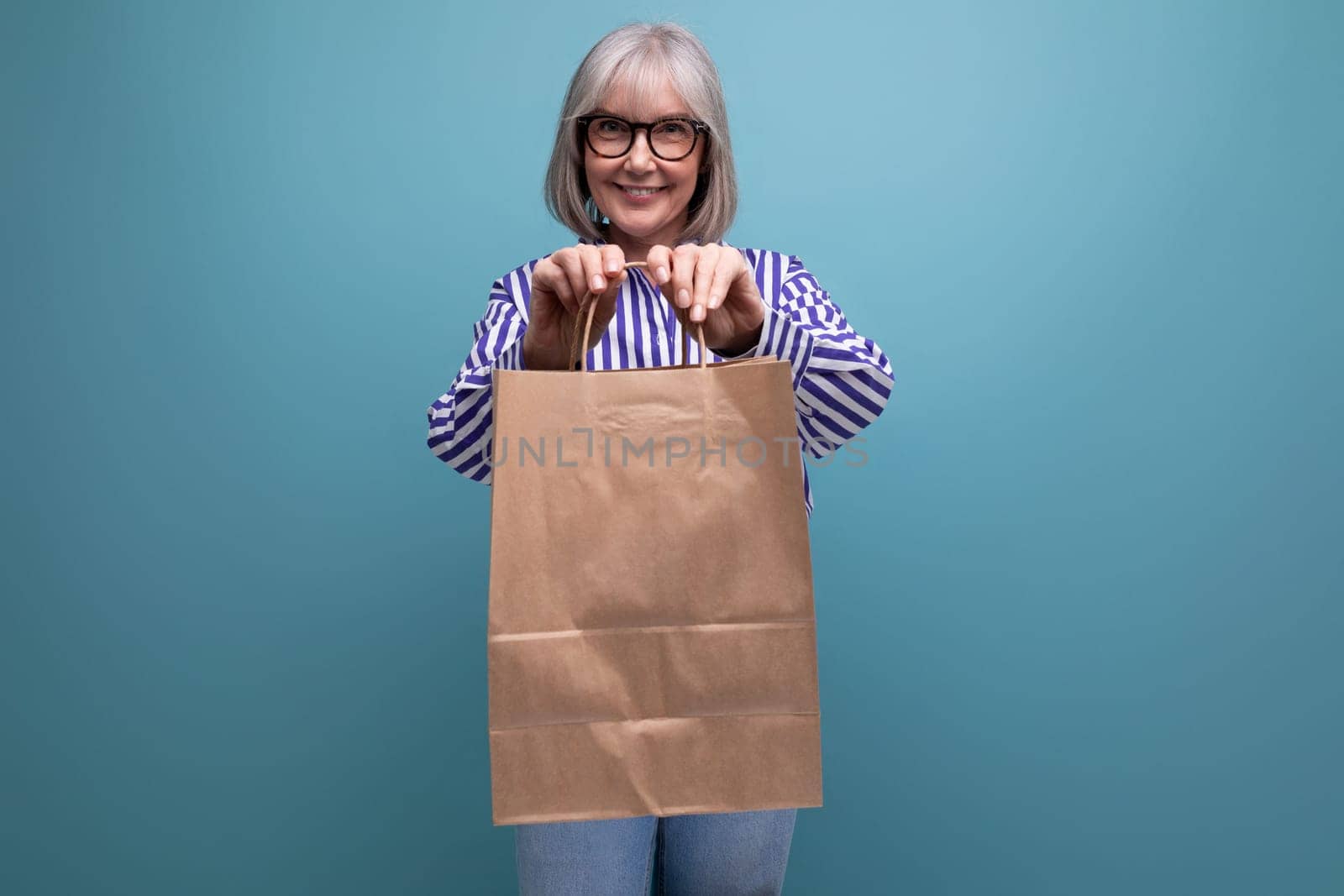 happy 60s middle aged woman with gray hair holding shopping bag on bright studio background with copy space.