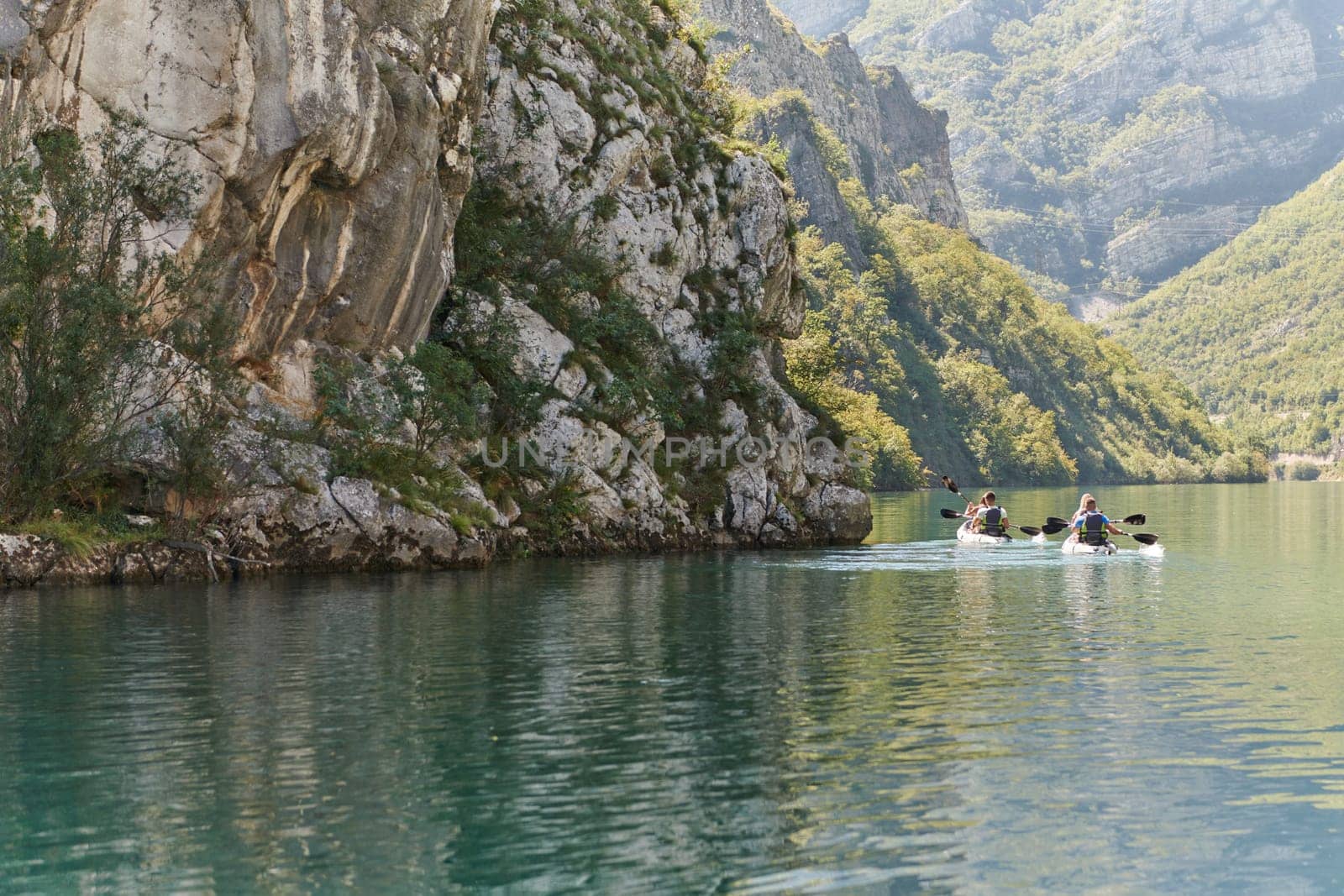 A group of friends enjoying having fun and kayaking while exploring the calm river, surrounding forest and large natural river canyons by dotshock