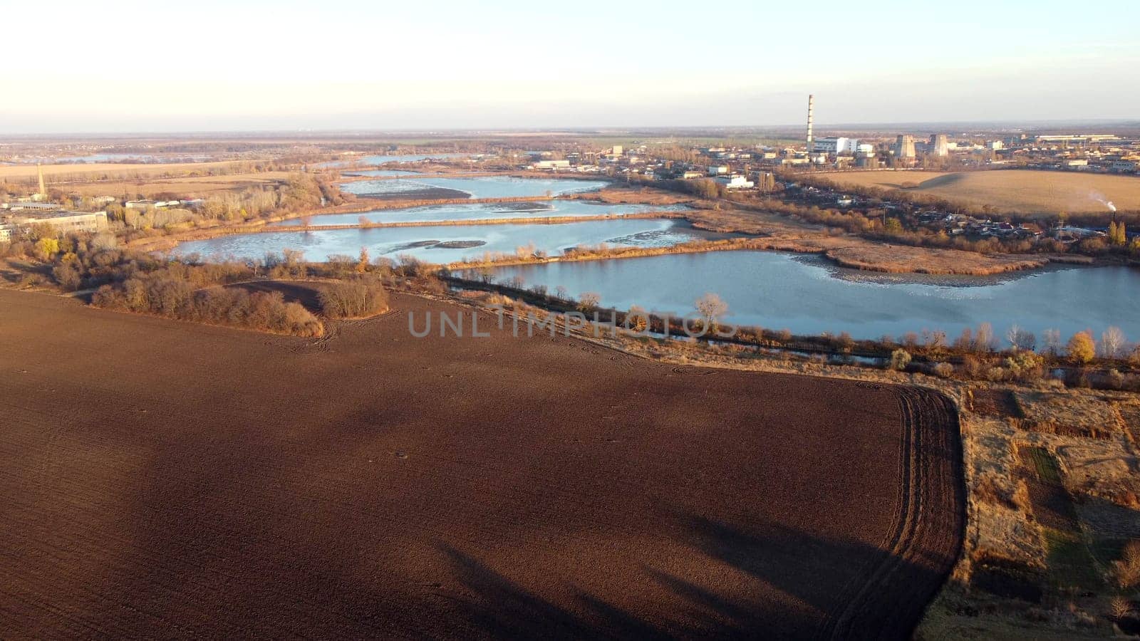 Urban beautiful landscape agricultural plowed fields, lakes for growing fish, gardens, thermal power plant, building industrial area of city on a sunny autumn day. Aerial drone view. Agrarian scenery