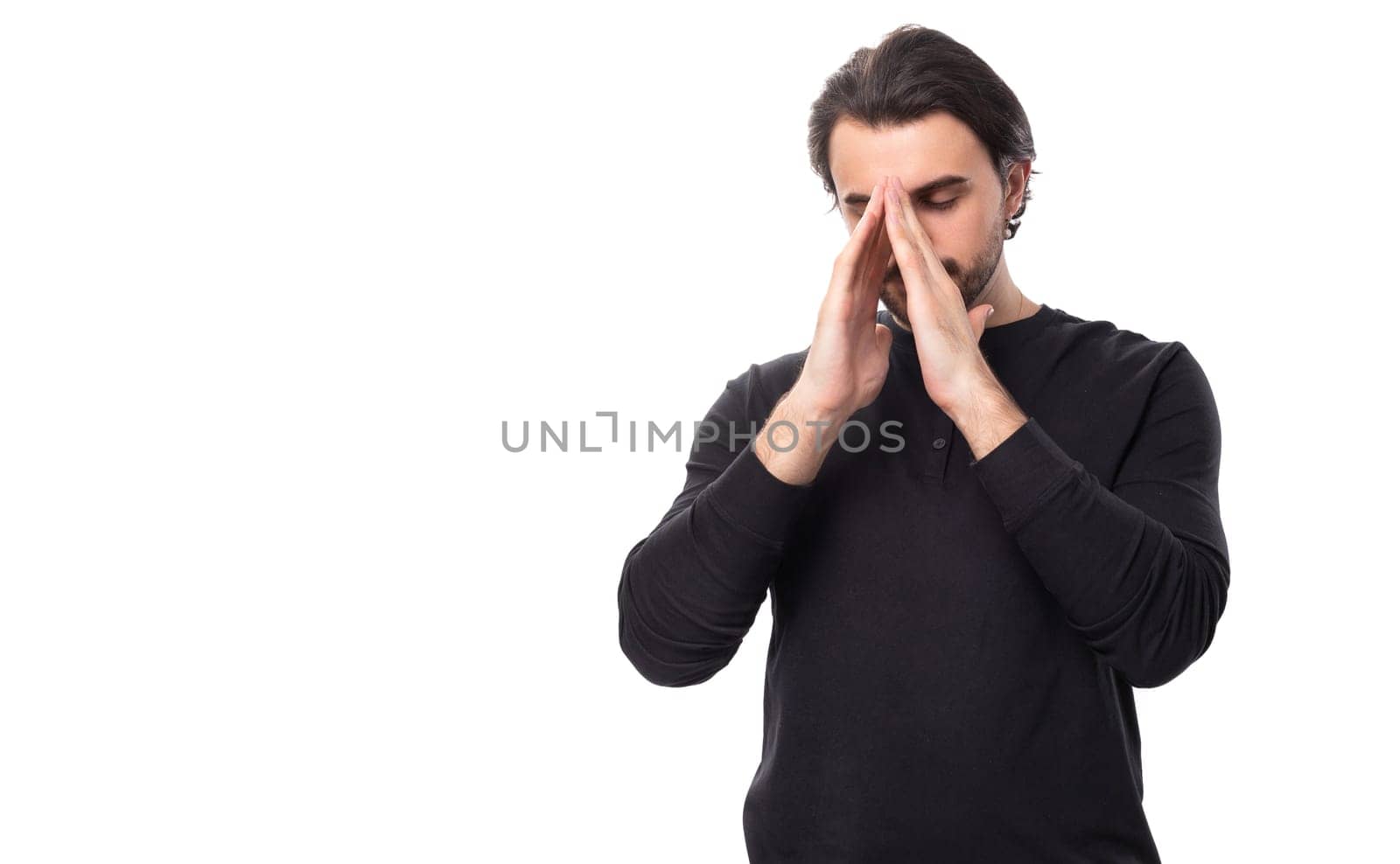 handsome brutal european macho man with black hair and beard with an earring in his ear hopes and prays waiting for good luck on an isolated white background with copy space by TRMK