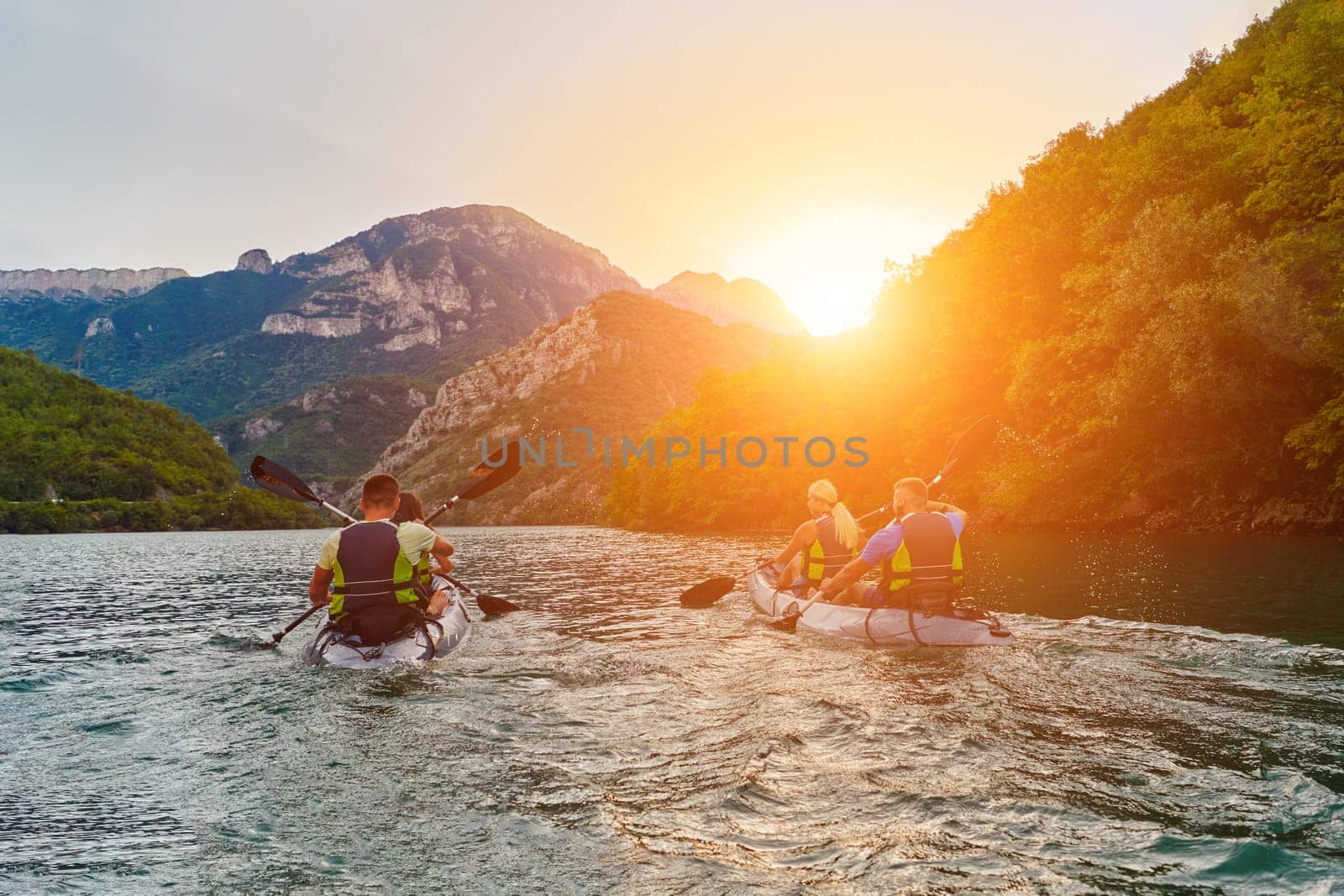 A group of friends enjoying fun and kayaking exploring the calm river, surrounding forest and large natural river canyons during an idyllic sunset. by dotshock