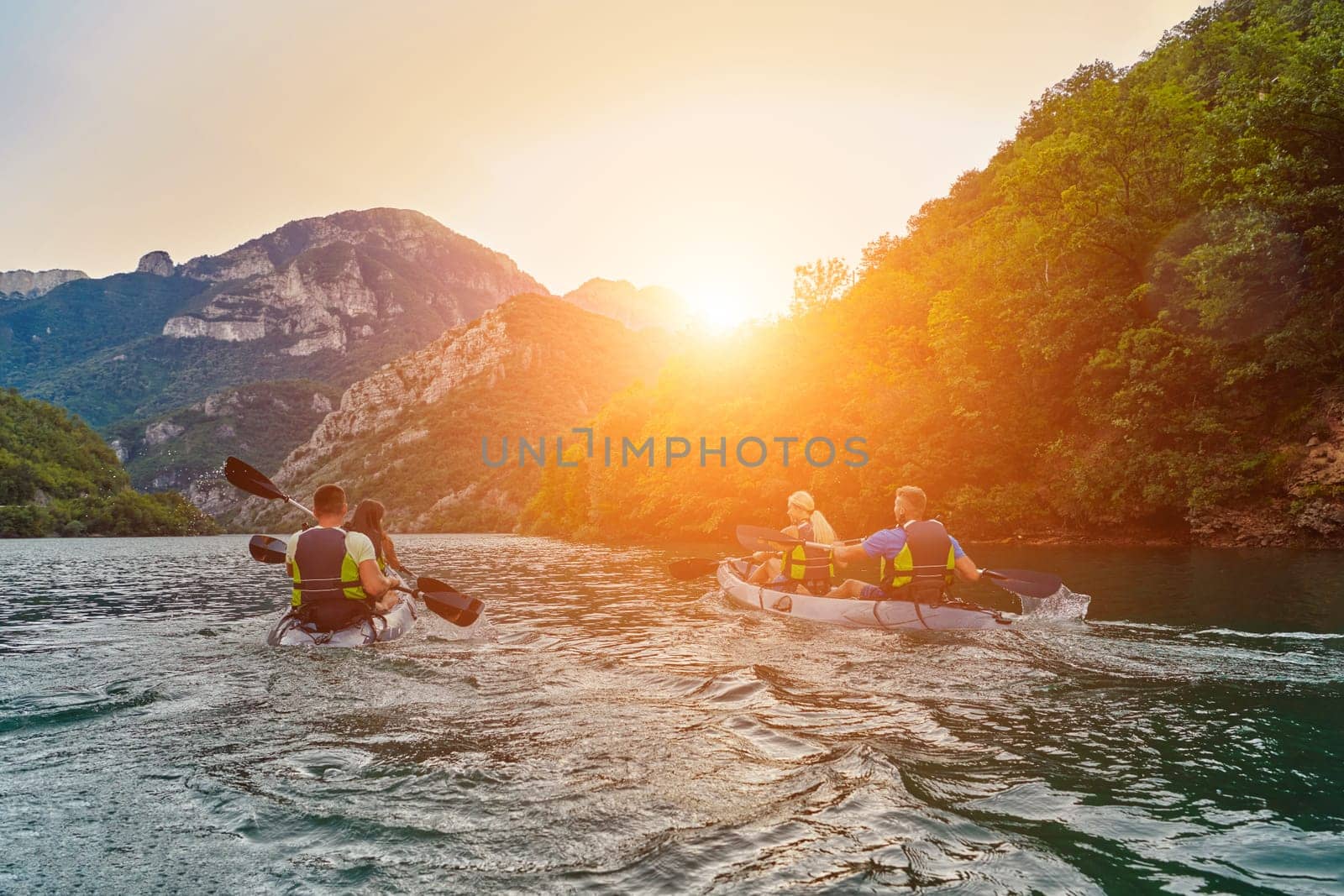 A group of friends enjoying fun and kayaking exploring the calm river, surrounding forest and large natural river canyons during an idyllic sunset