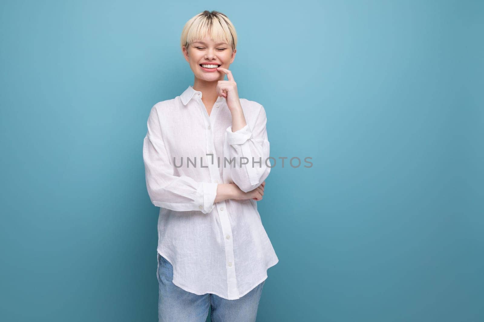 young pretty caucasian office worker woman with short blond hair is dressed in a white blouse on a blue background with copy space. business concept.