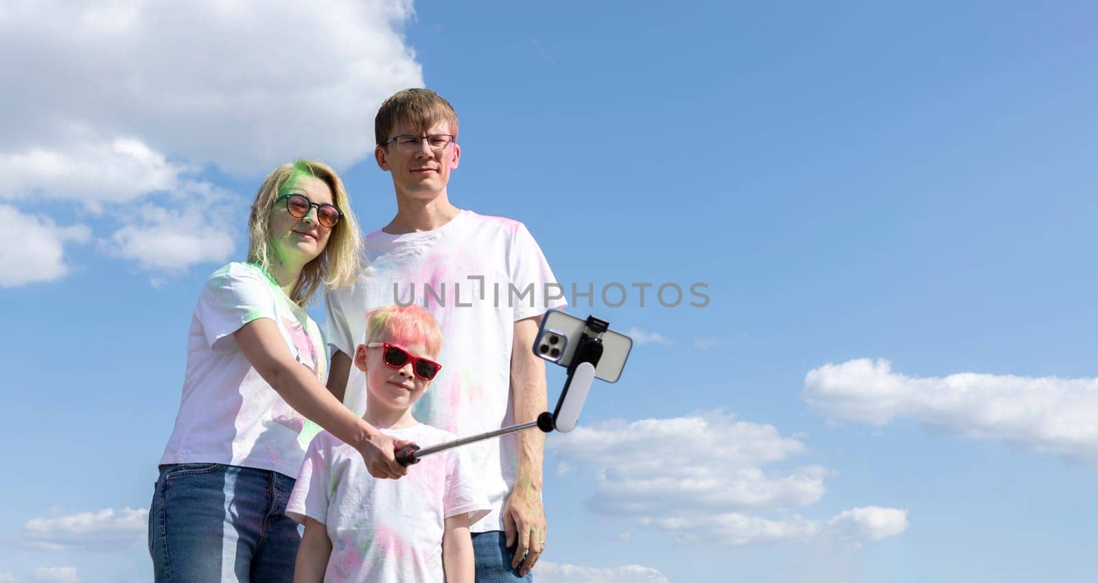 Caucasian Family Takes Selfie. Parent And Child With Colorful Dye At Birthday Party Or Celebrating Holi Color Festival, Blue Sky On background. Cheerful Family Spend Time Together. Horizontal Plane.