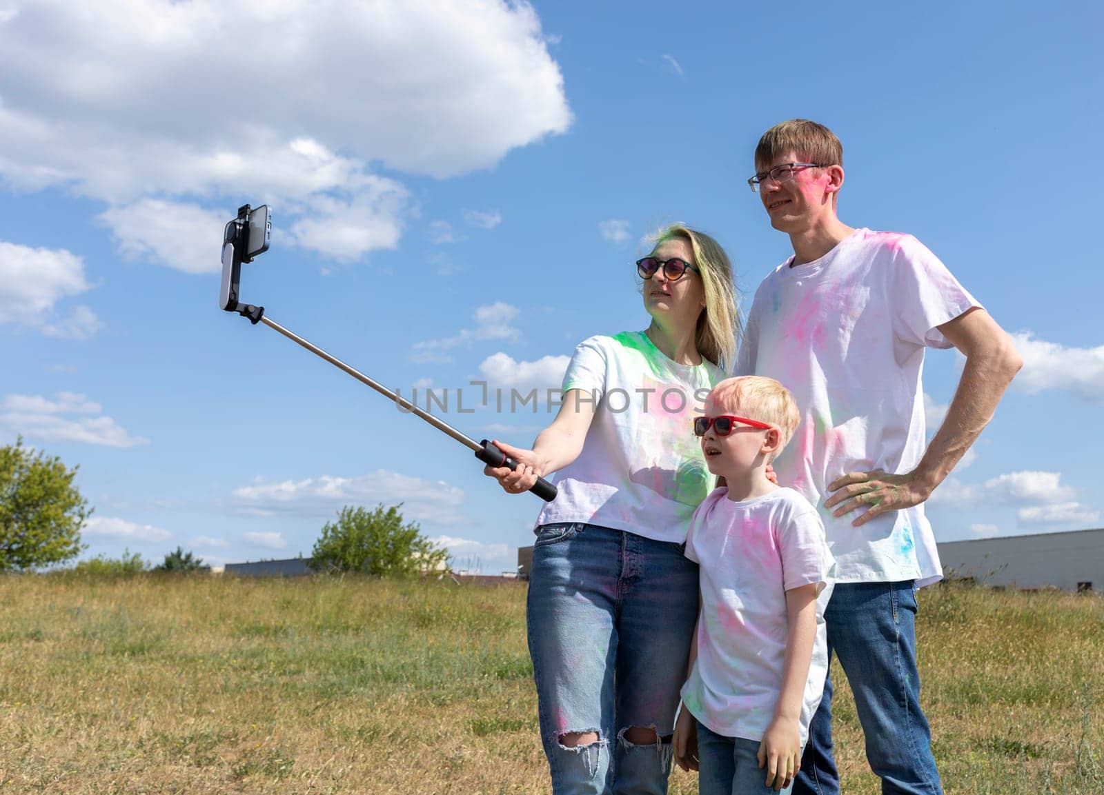 Caucasian Family Takes Selfie. Parent, Child With Colorful Dye At Birthday Party Or Celebrating Holi Color Festival, Blue Sky On background. Cheerful Family Spend Time Together. Horizontal Copy Space