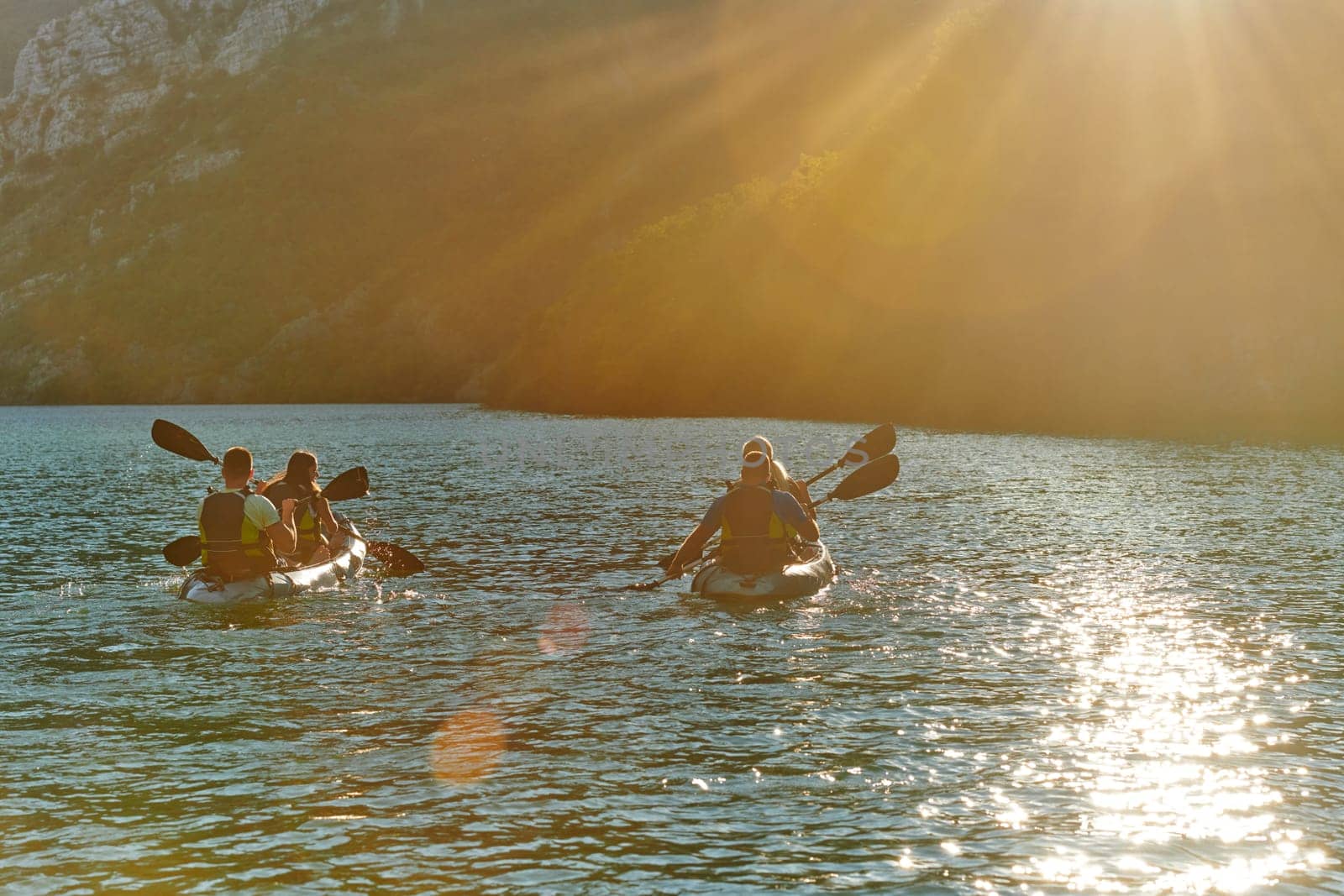 A group of friends enjoying fun and kayaking exploring the calm river, surrounding forest and large natural river canyons during an idyllic sunset. by dotshock