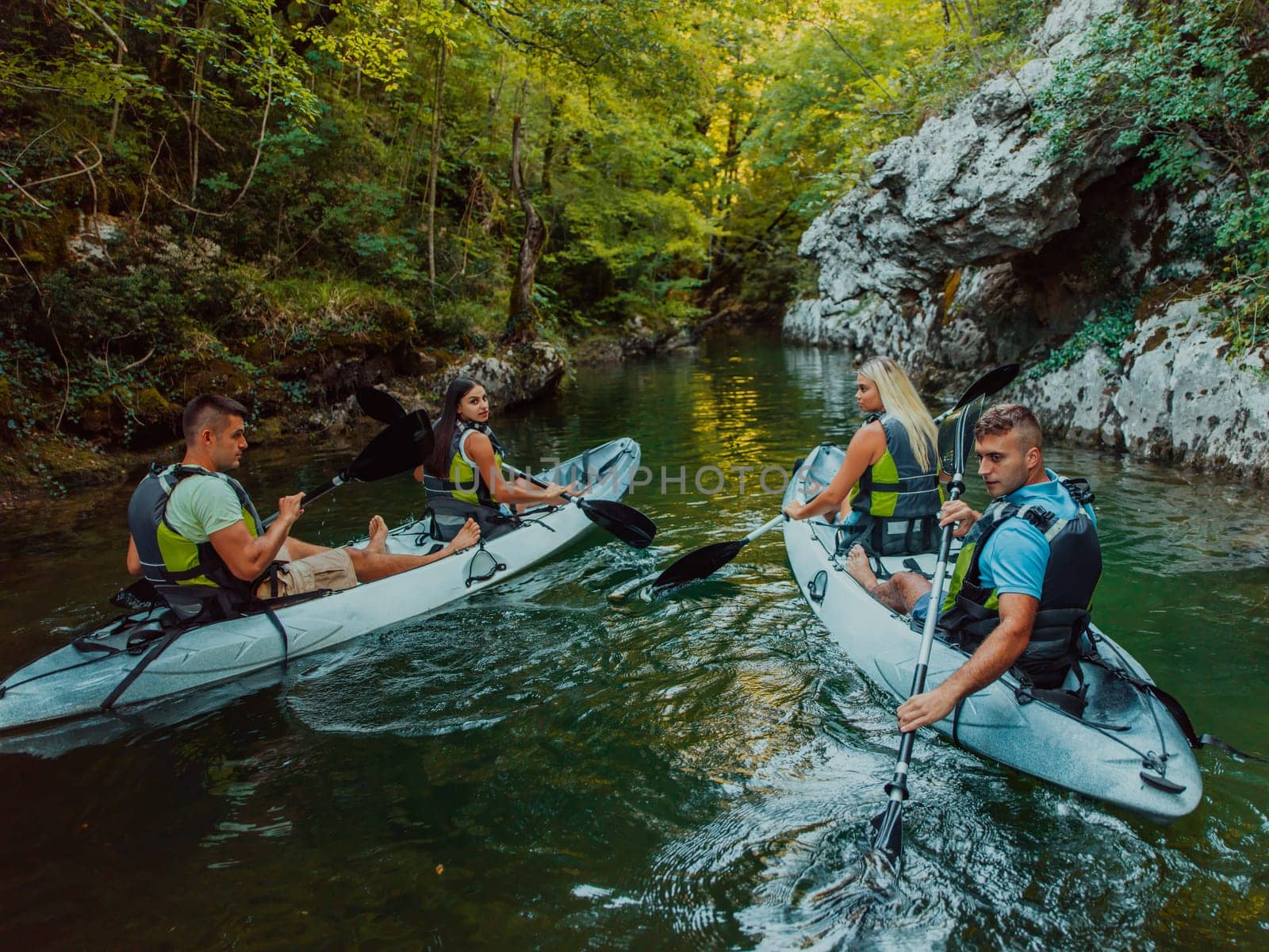 A group of friends enjoying having fun and kayaking while exploring the calm river, surrounding forest and large natural river canyons.