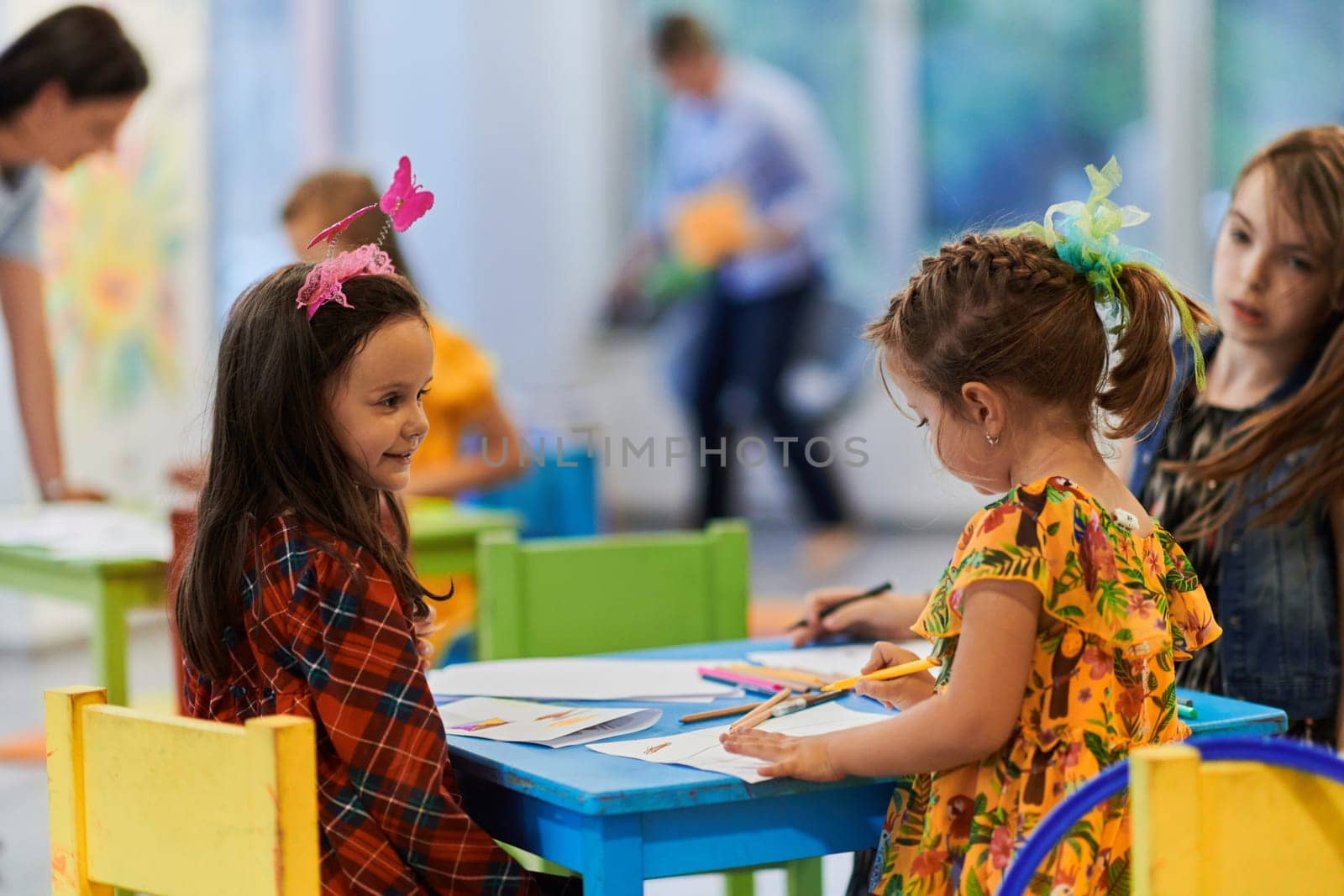 Creative kids during an art class in a daycare center or elementary school classroom drawing with female teacher