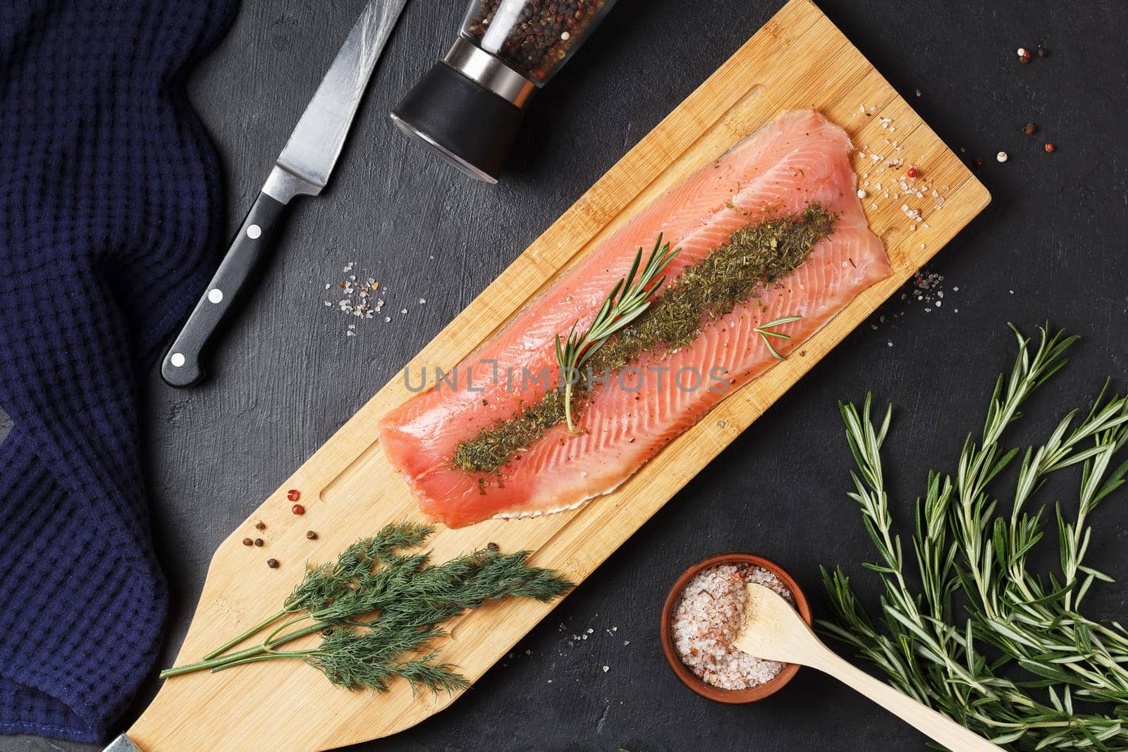Salted fish fillet with spices and herbs:dill and rosemary on a wooden board on a black background.