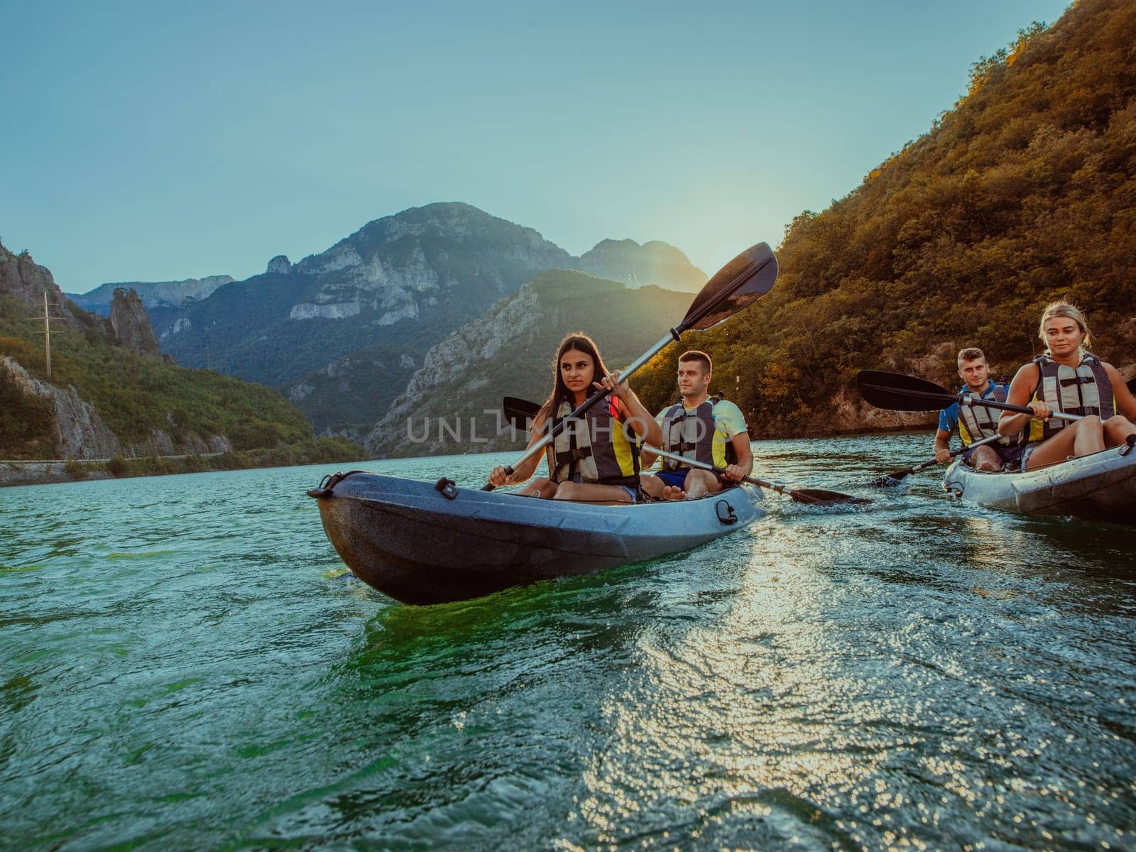 A group of friends enjoying fun and kayaking exploring the calm river, surrounding forest and large natural river canyons during an idyllic sunset