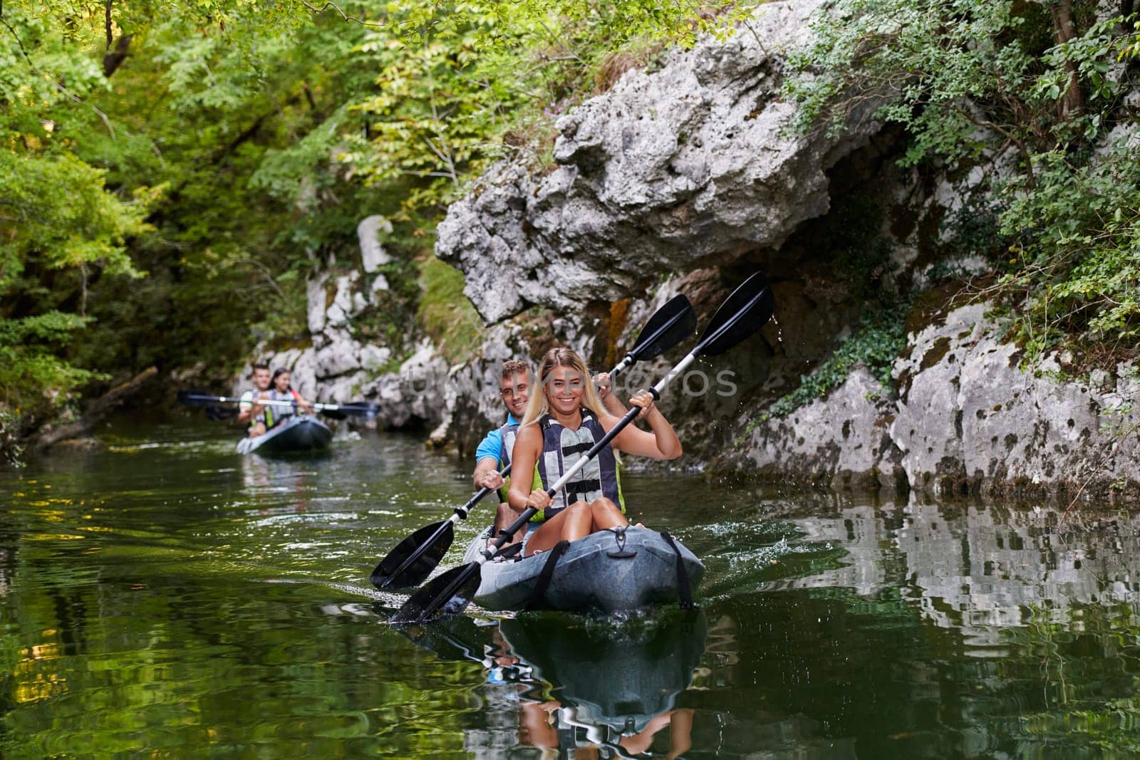 A group of friends enjoying having fun and kayaking while exploring the calm river, surrounding forest and large natural river canyons.