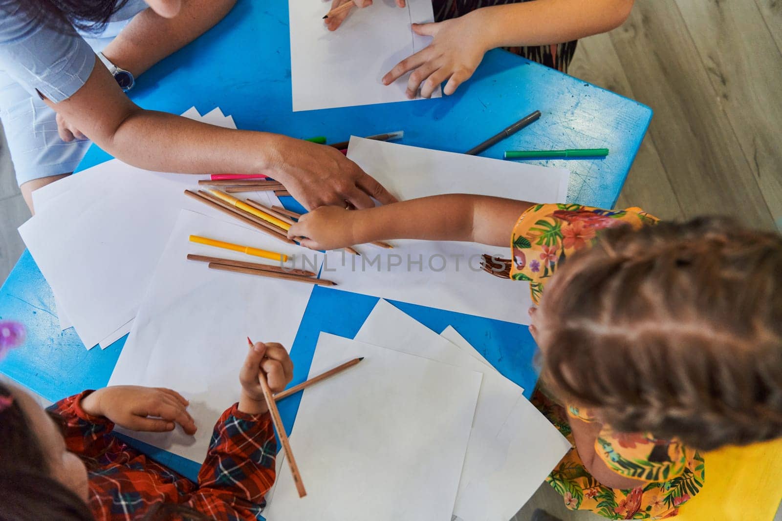 Creative kids during an art class in a daycare center or elementary school classroom drawing with female teacher