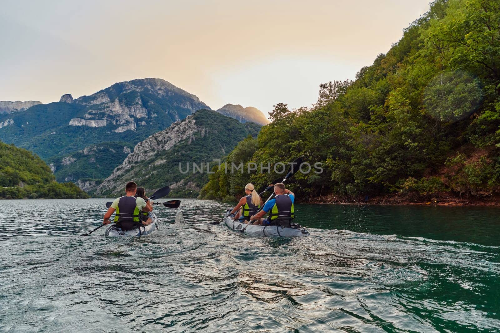 A group of friends enjoying fun and kayaking exploring the calm river, surrounding forest and large natural river canyons during an idyllic sunset