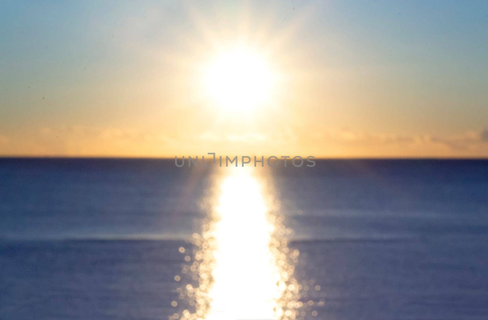 Blurred background. Sun shining in blue sky during sunset dawn. Sunrise dawning sundown. Sunny path, sunny walkway on surface of sea waves. Sunlight Sunbeams Sea landscape Natural blurry bokeh texture