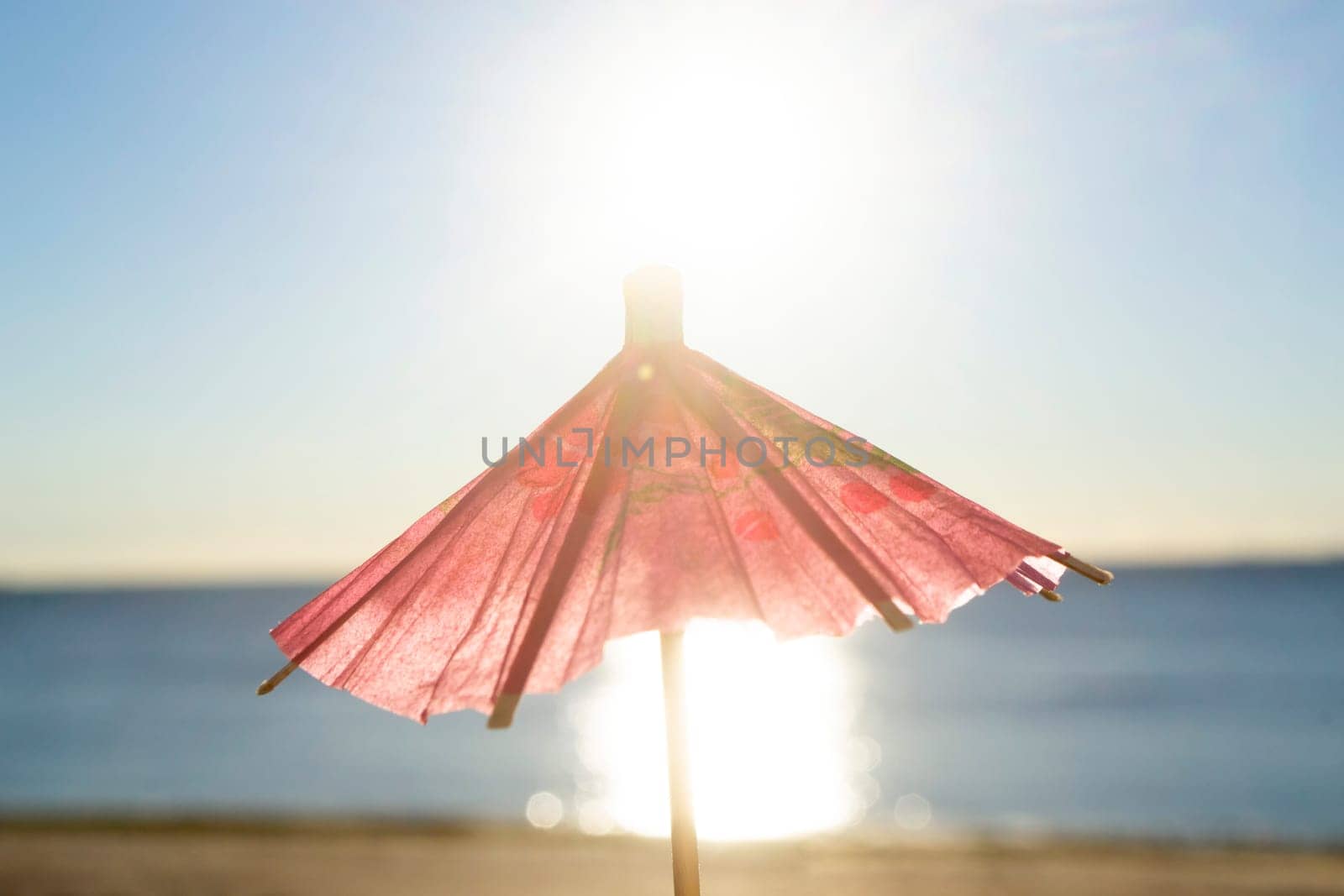 One red paper umbrellas cocktail decorations on background of blue sky, brightly shining sun and sunny path on surface of blue sea. Concept of summer, sea, vacation, travel tourism